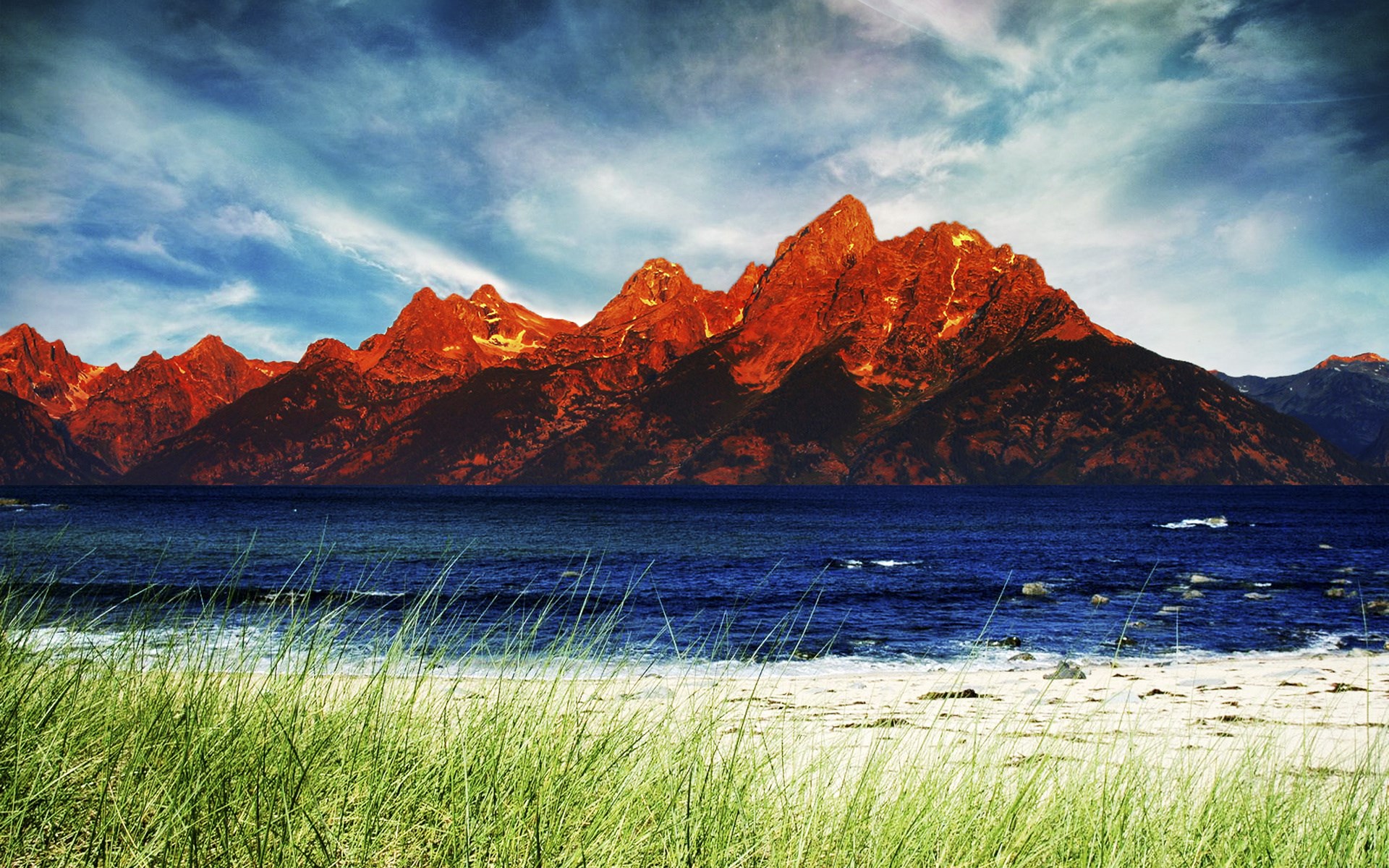 Red mountains over blue water and beach grass HD Wallpaper