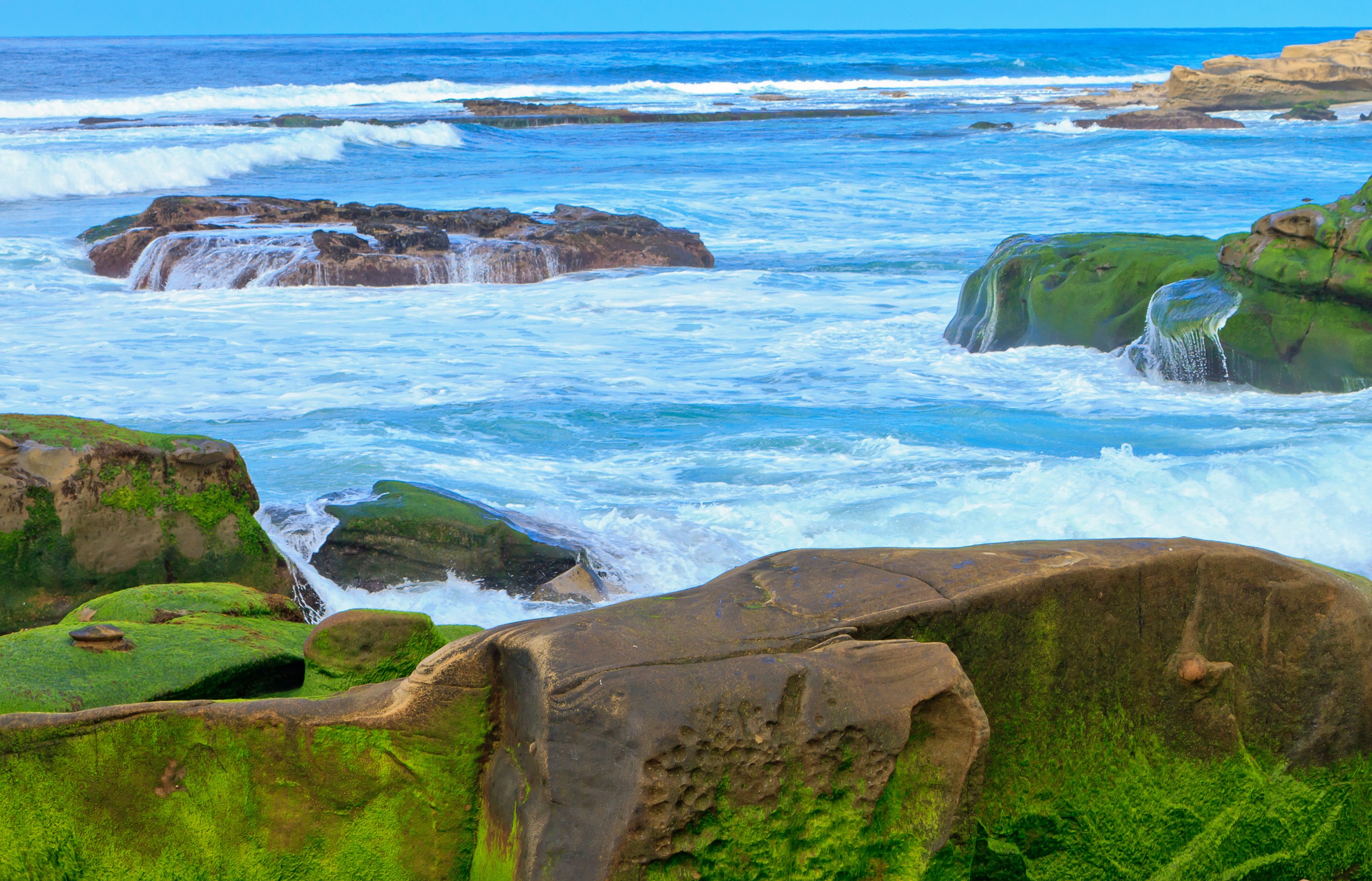 Ocean waves crashing on moss-covered rocks HD Wallpaper