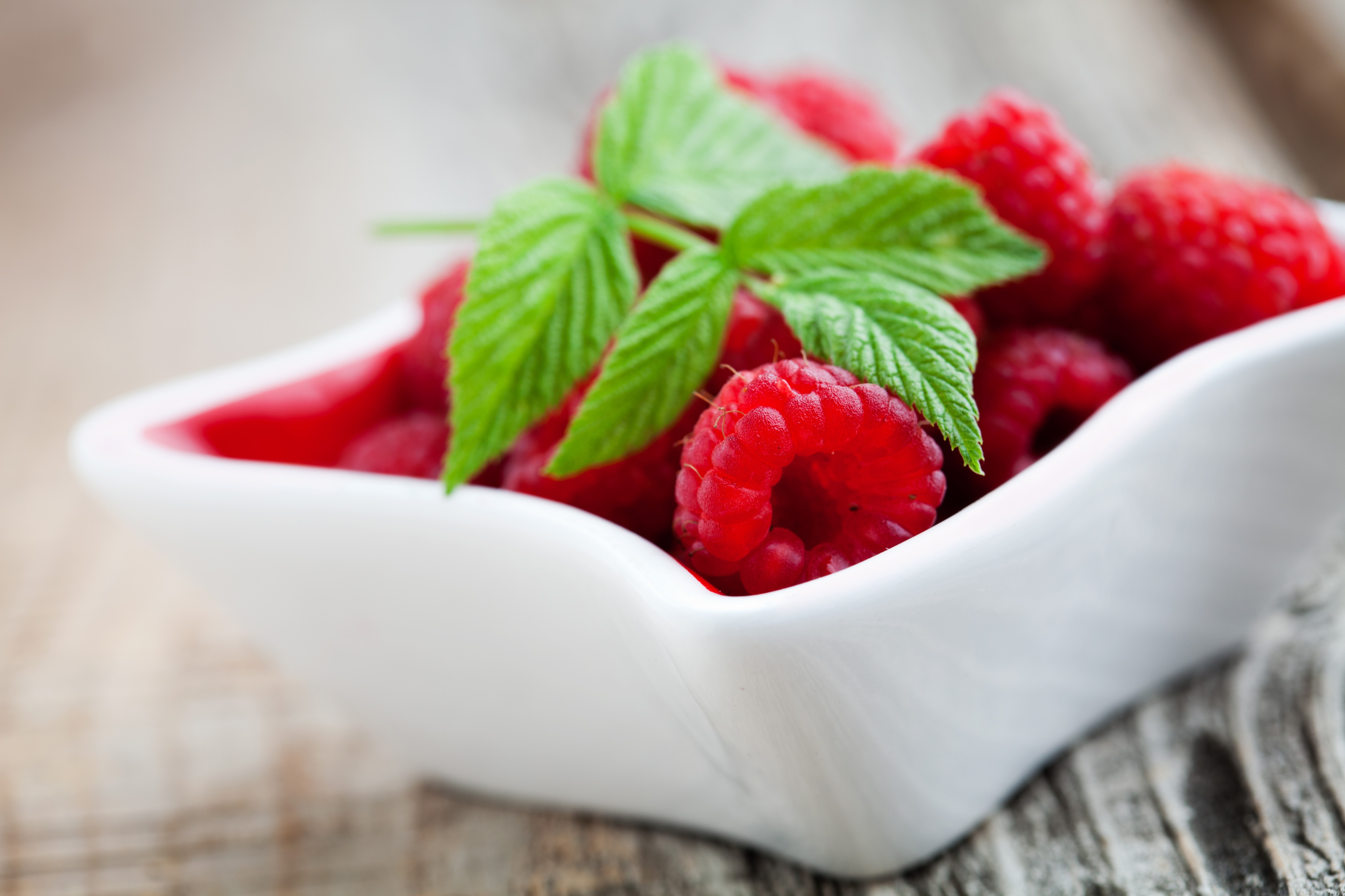 Raspberries in a white bowl with green leaves HD Wallpaper