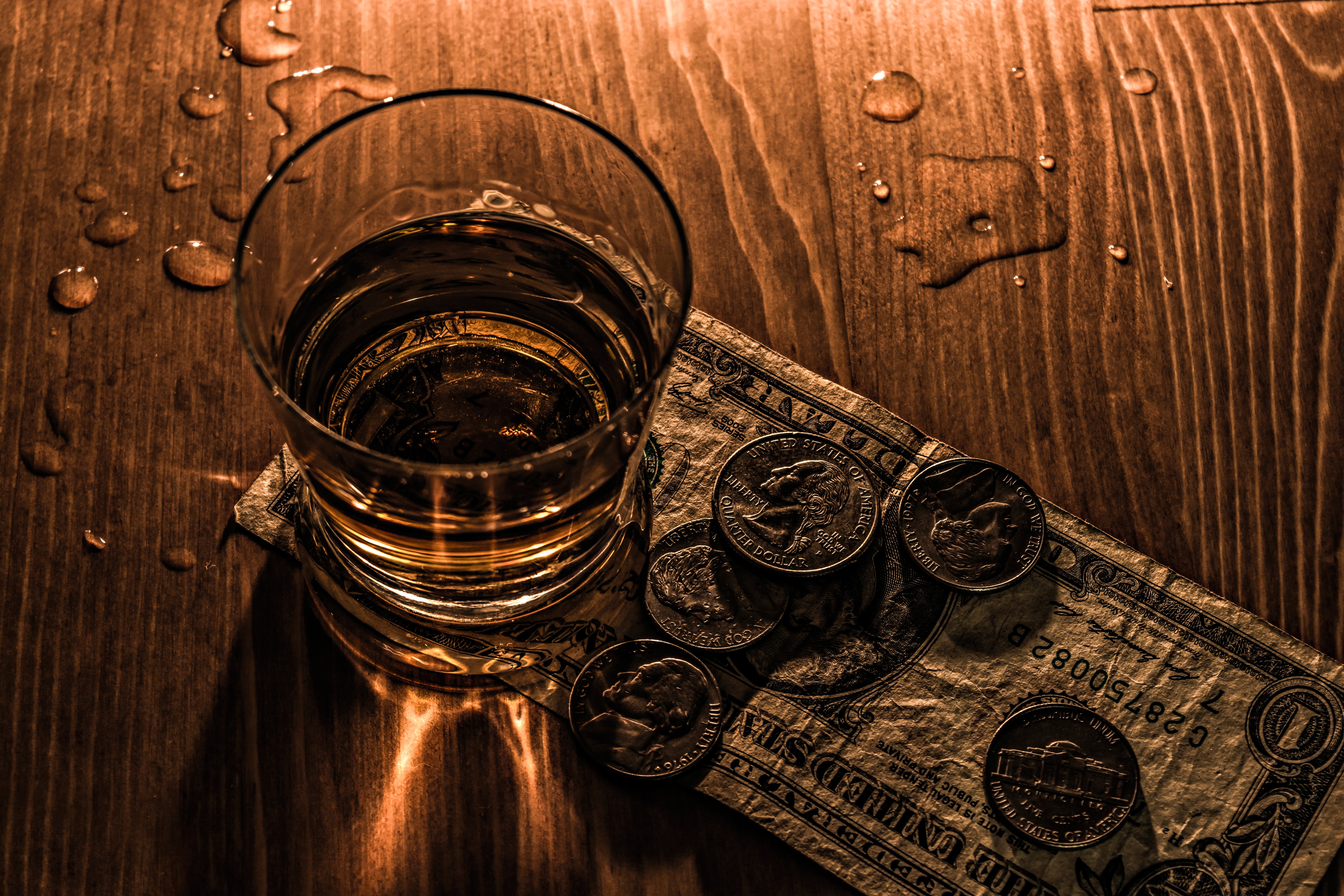 Glass of whiskey with money and coins on a wooden table HD Wallpaper