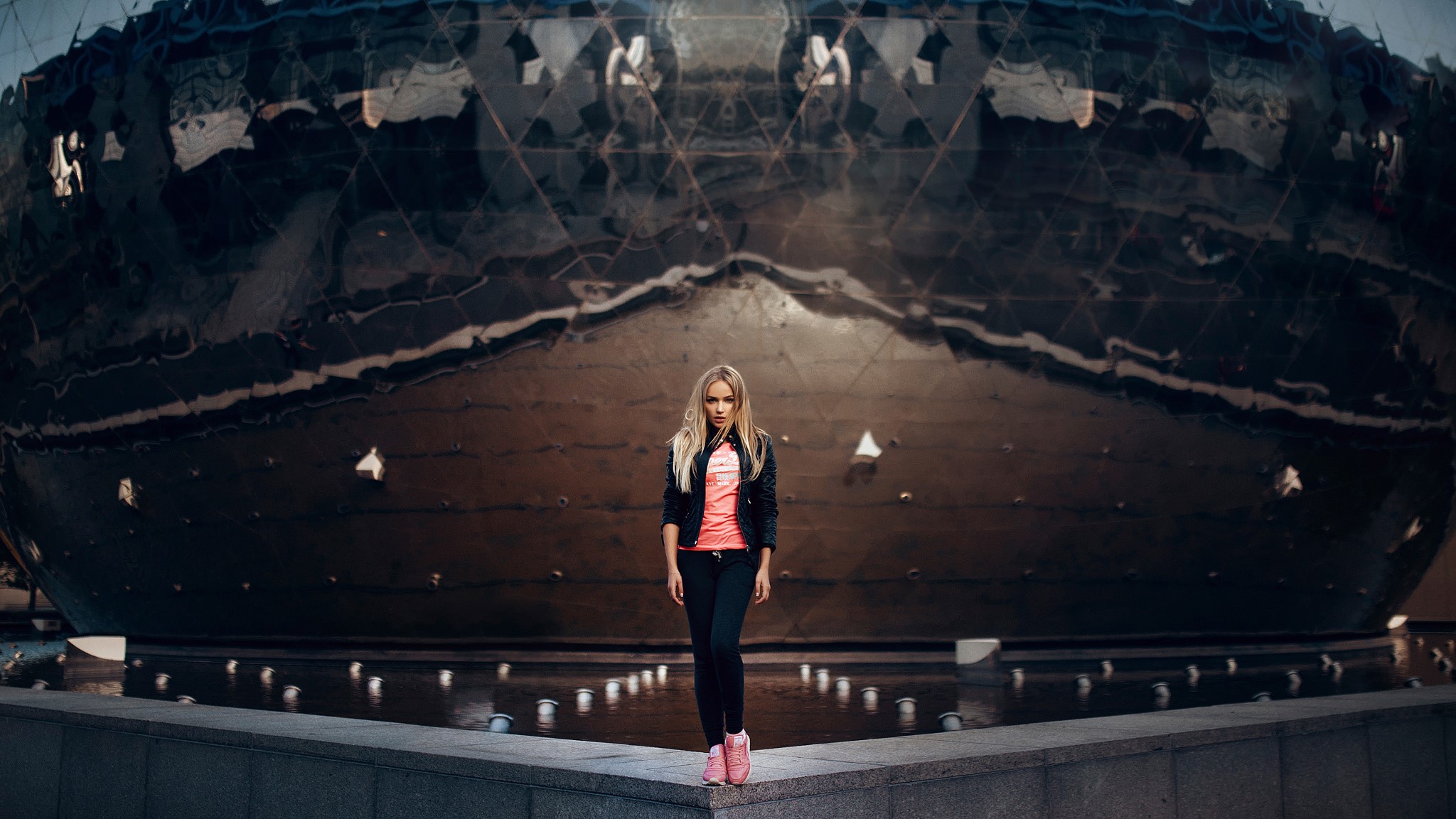 Woman in black jacket and pink top near a large spherical building with fountains HD Wallpaper