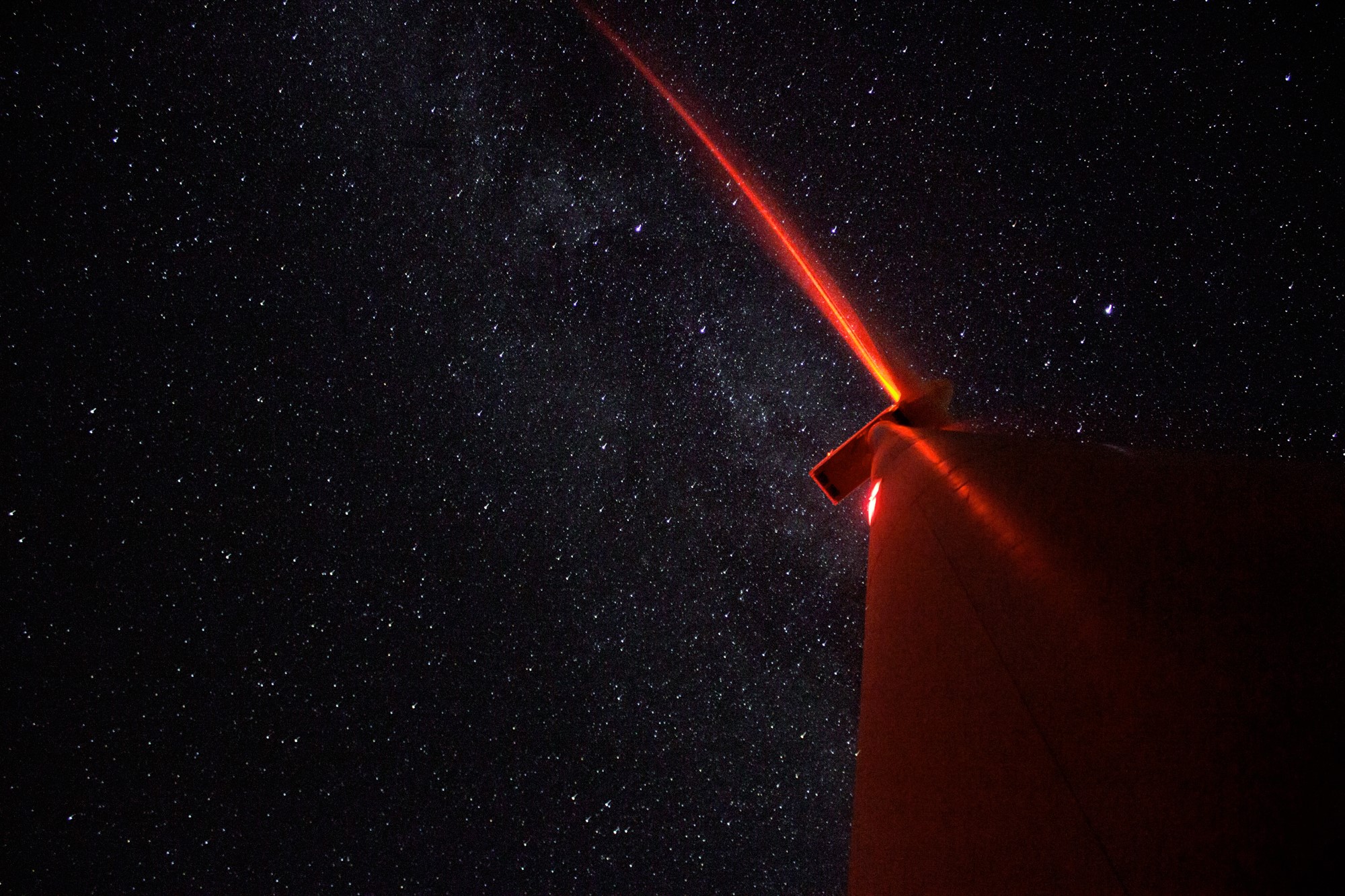 Red beam of light from a structure against a starry night sky HD Wallpaper