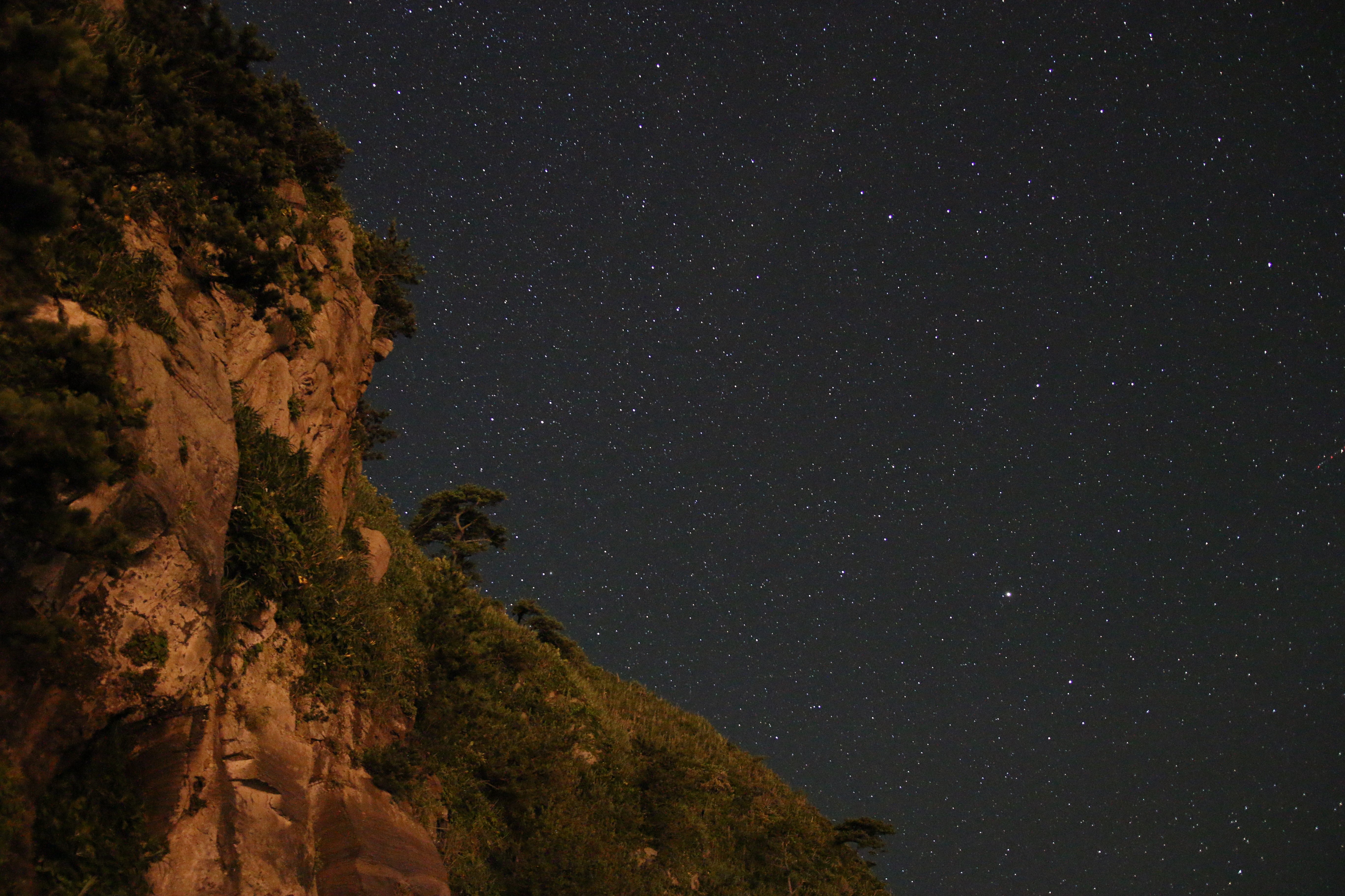 Night sky with stars over a rocky cliffside HD Wallpaper