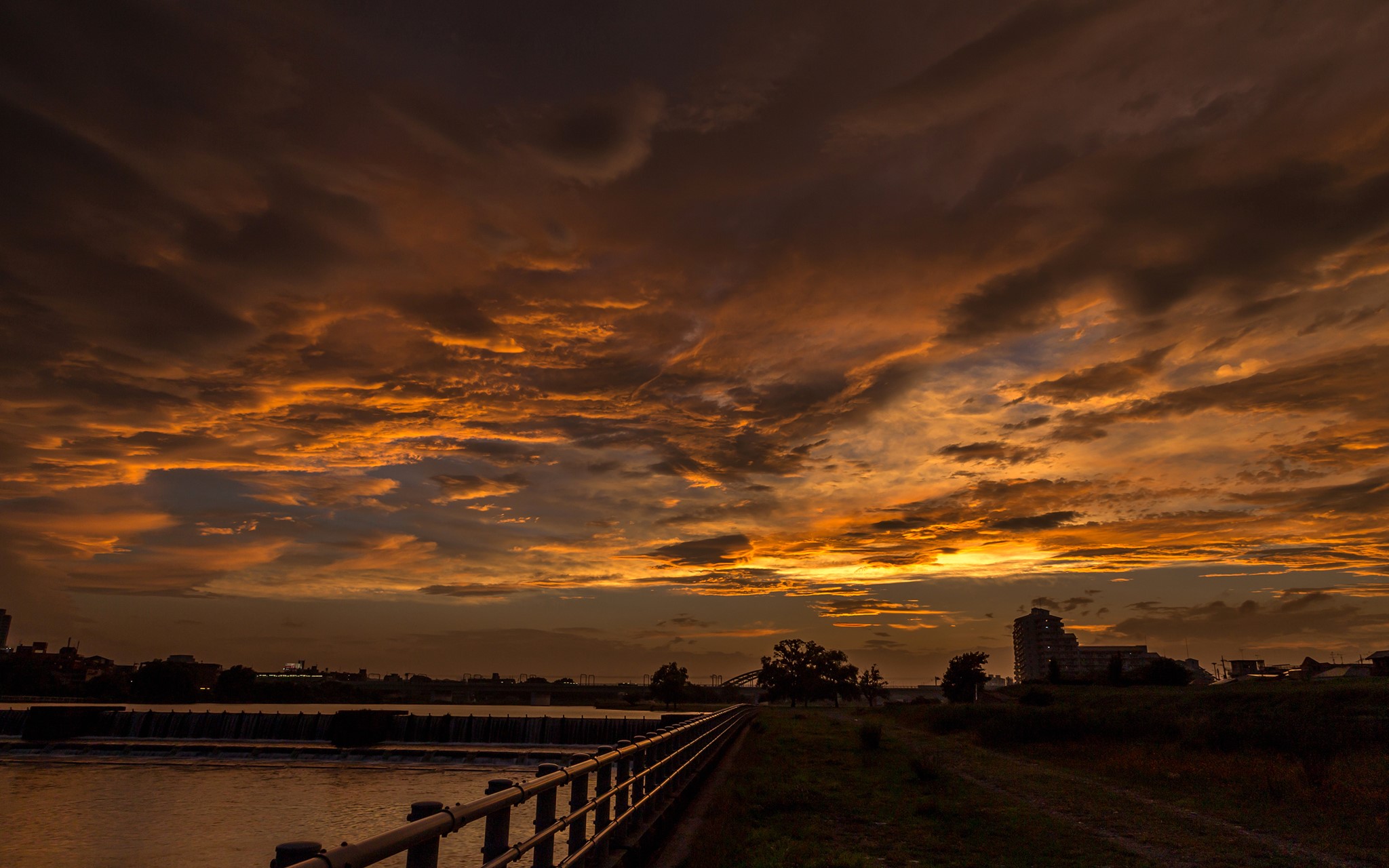 Sunset over a river with a fence and buildings HD Wallpaper