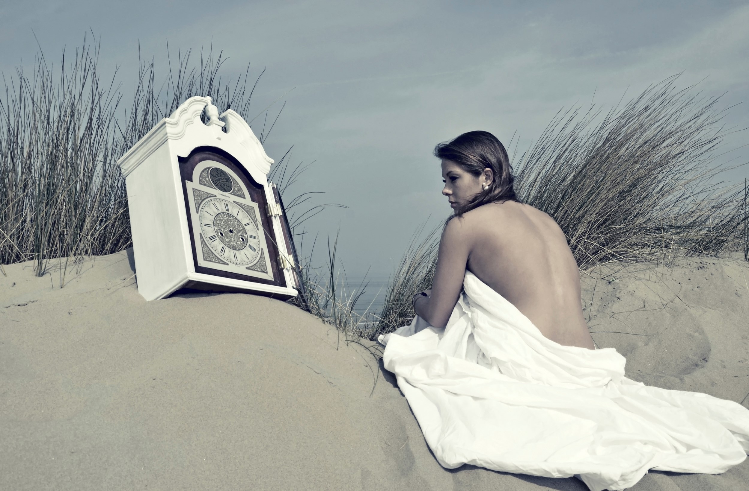 Woman and grandfather clock on a sandy beach HD Wallpaper