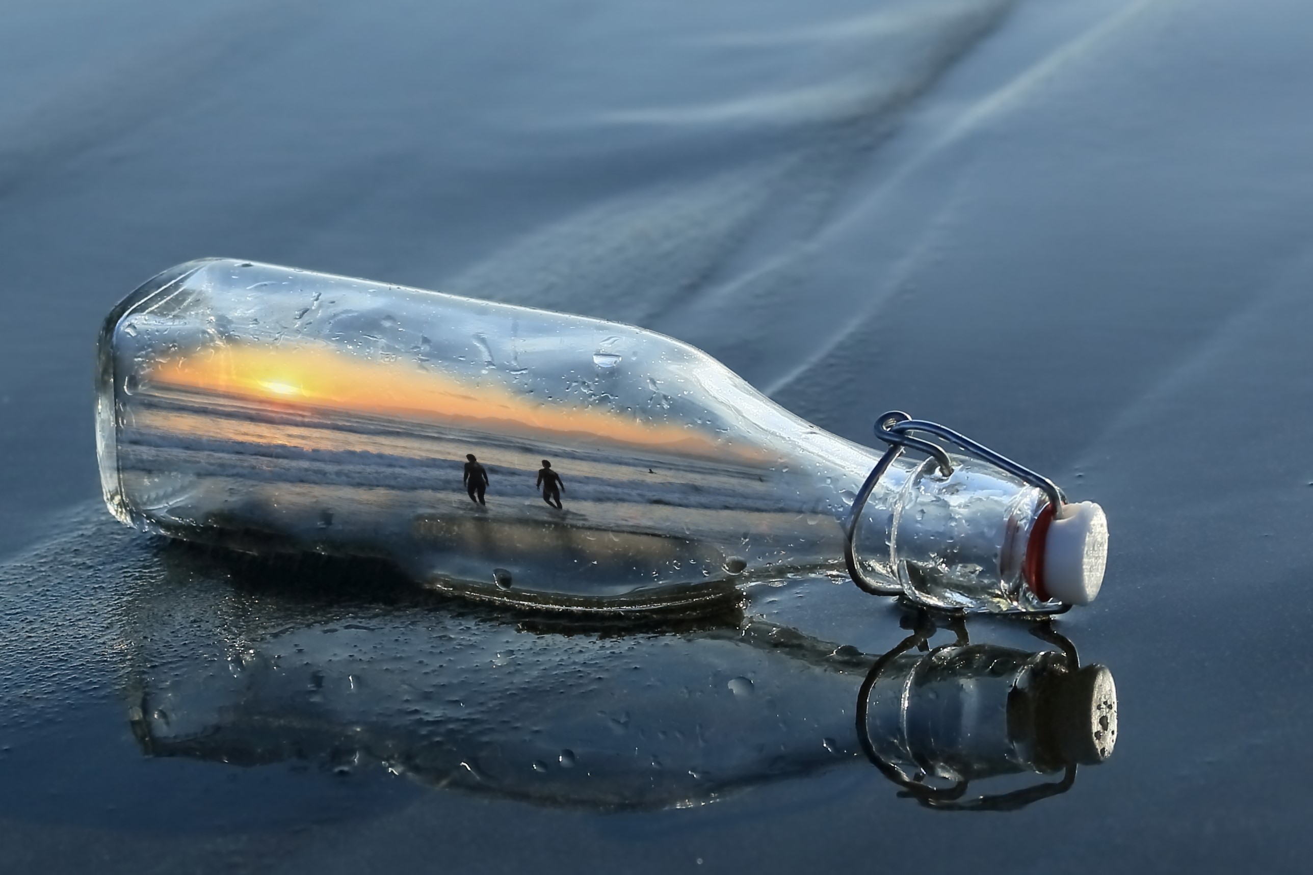 Bottle with sunset reflection and two people on beach HD Wallpaper