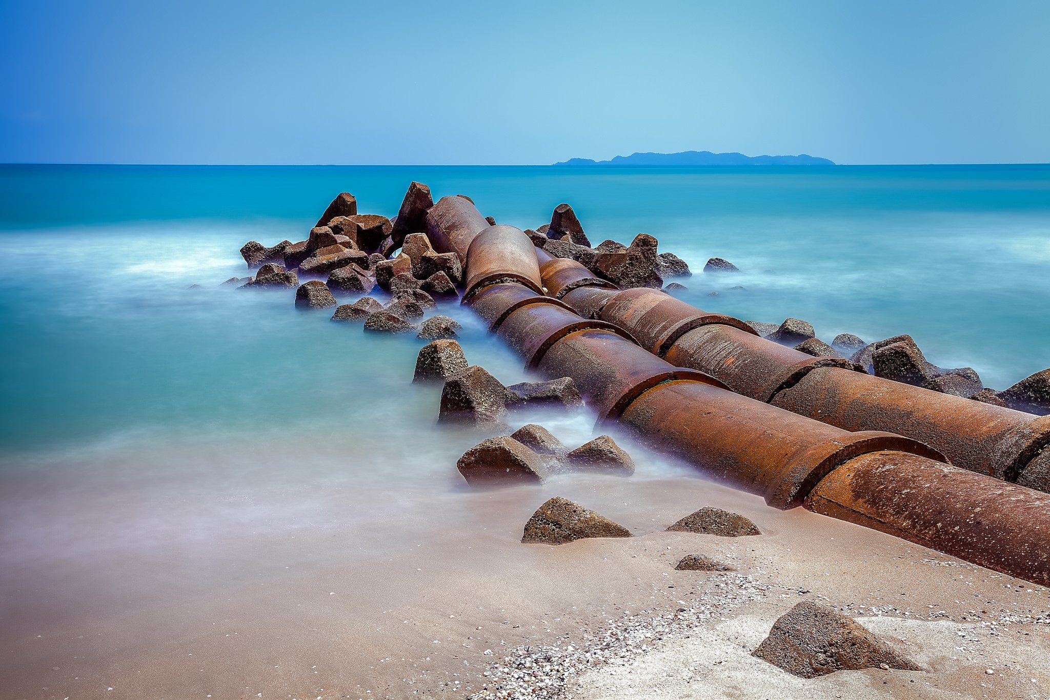 Rusty pipes and tetrapods on a beach with the sea HD Wallpaper