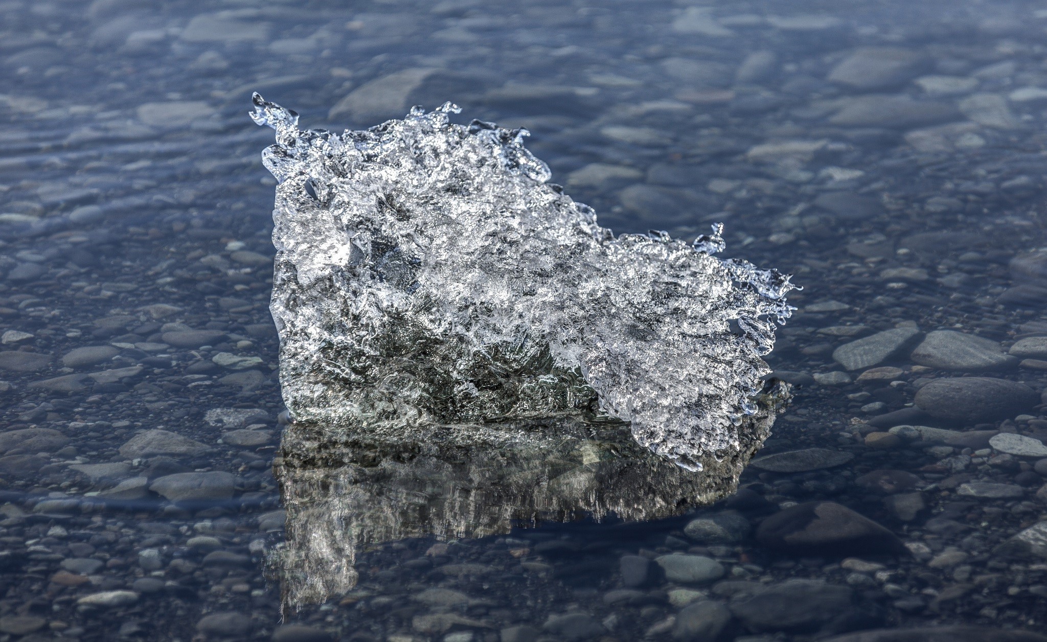 Ice fragment floating in shallow water with pebbles HD Wallpaper