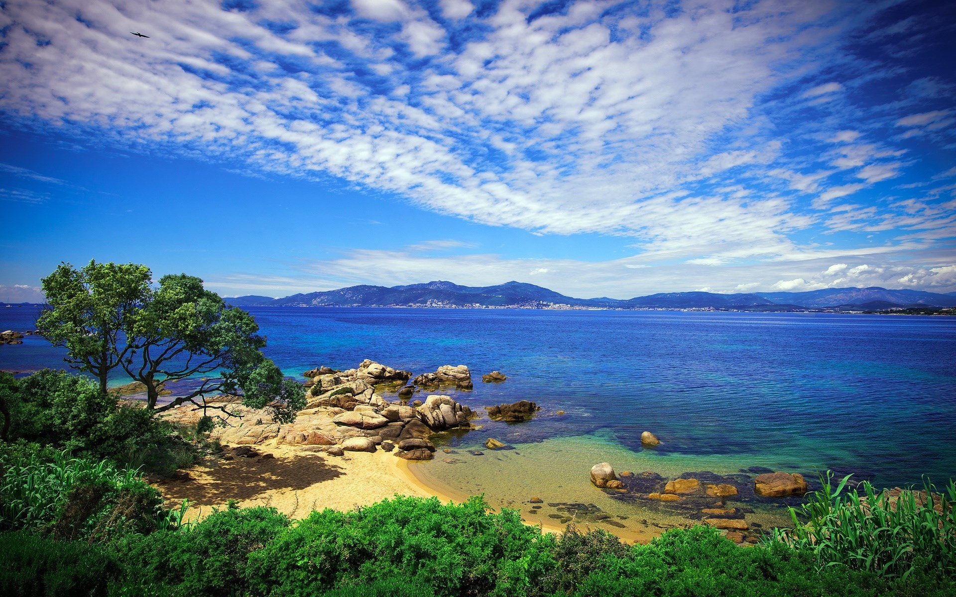 Coastal landscape with rocky beach and distant mountains HD Wallpaper