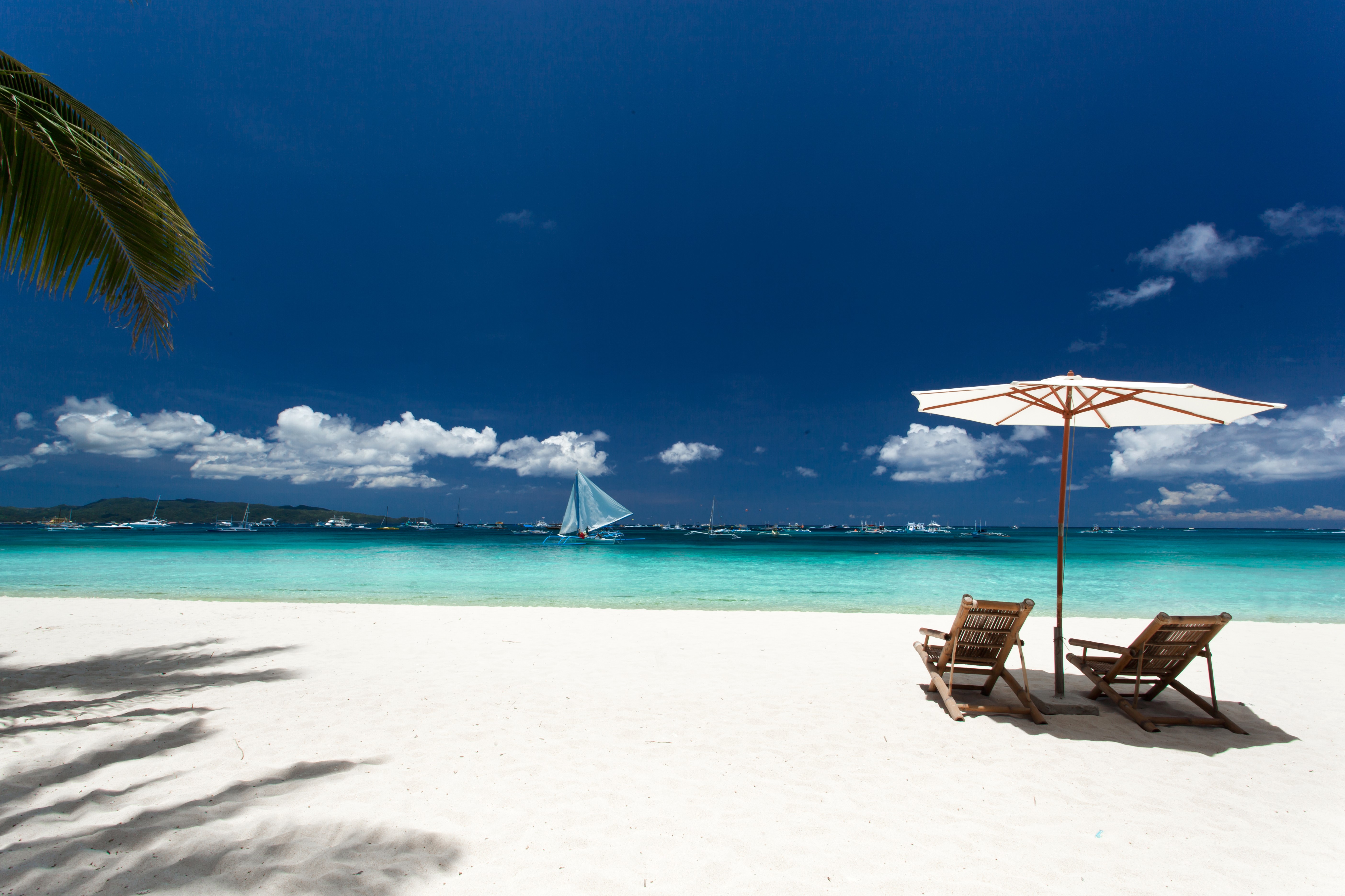 Tropical beach with sailboats and lounge chairs HD Wallpaper
