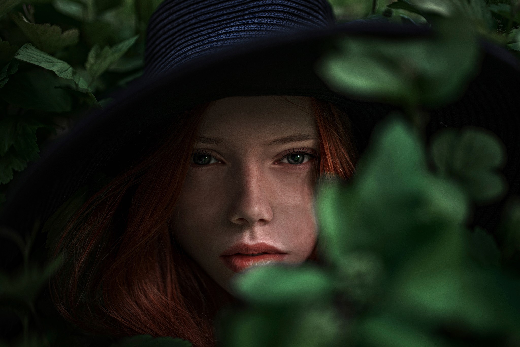 Woman in a wide-brimmed hat peeking through leaves HD Wallpaper