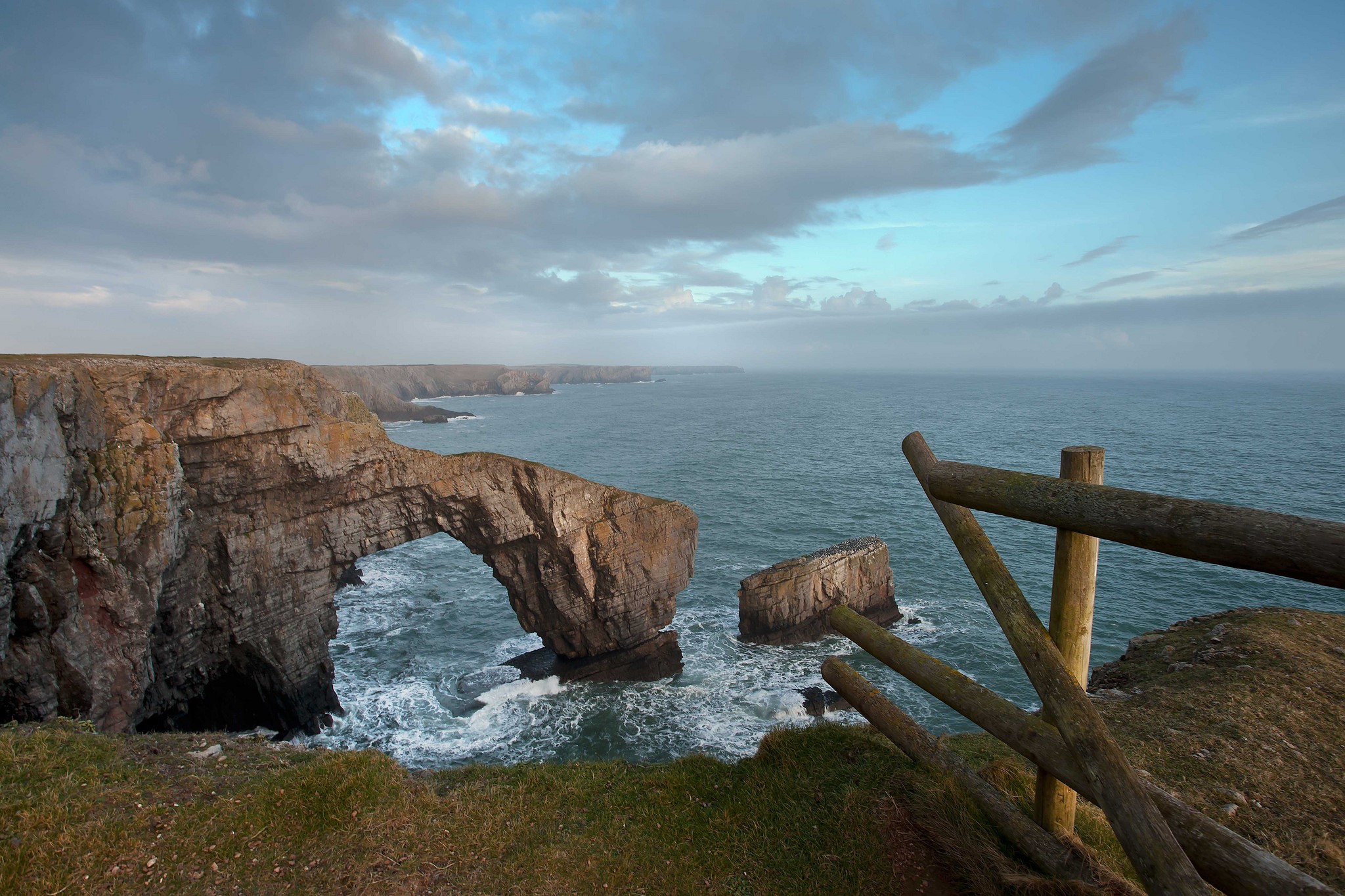 Rocky coast with sea arch and wooden fence HD Wallpaper