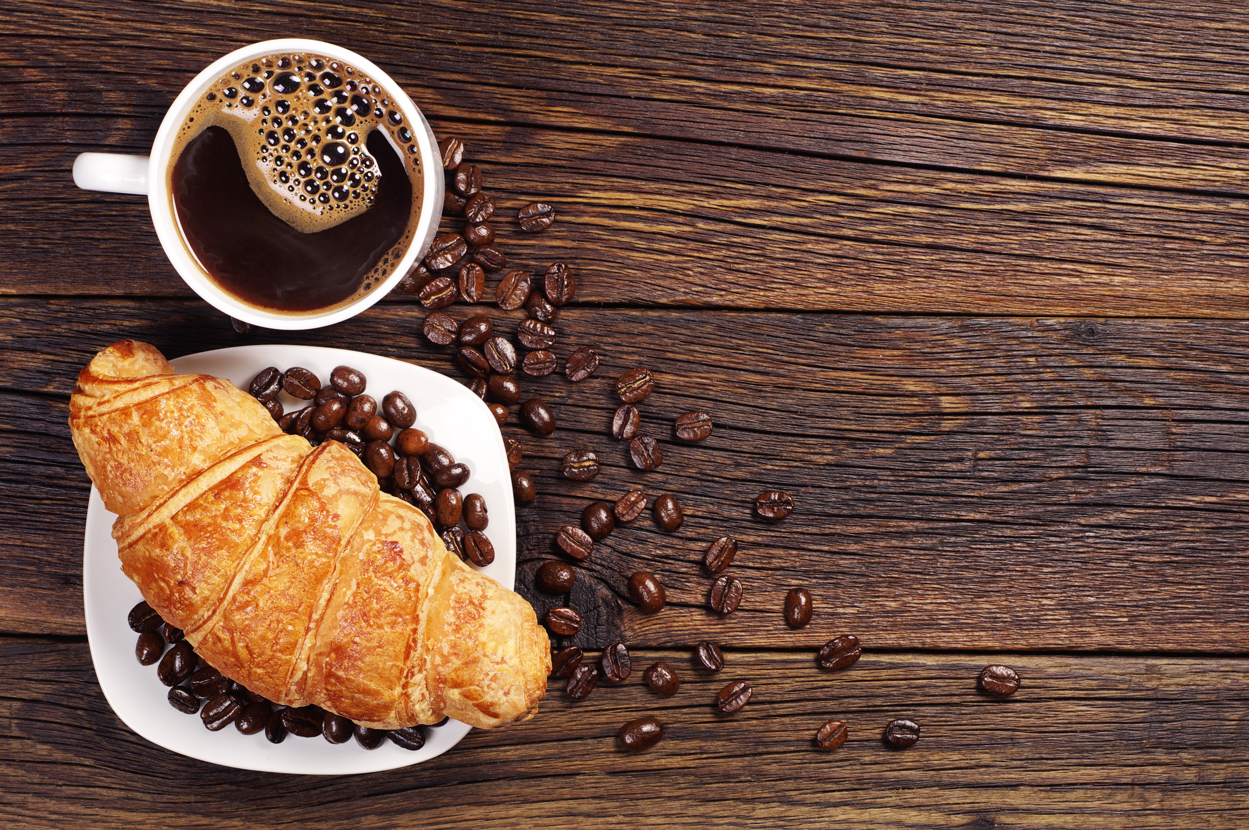 Croissant and coffee with beans on wooden table HD Wallpaper
