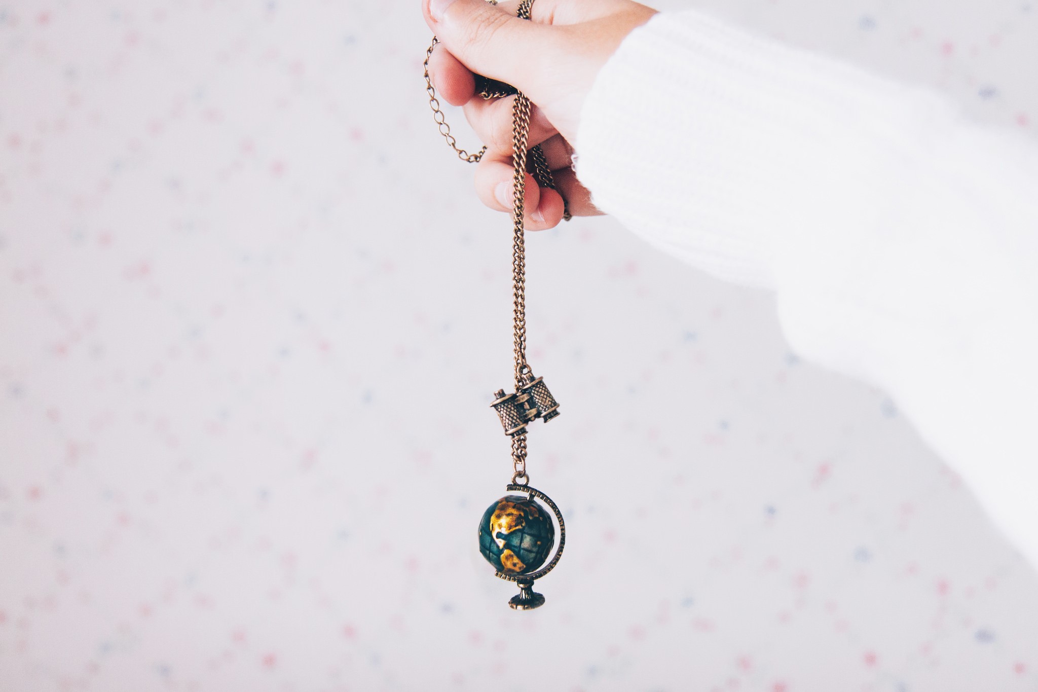 Hand holding a necklace with a globe pendant HD Wallpaper