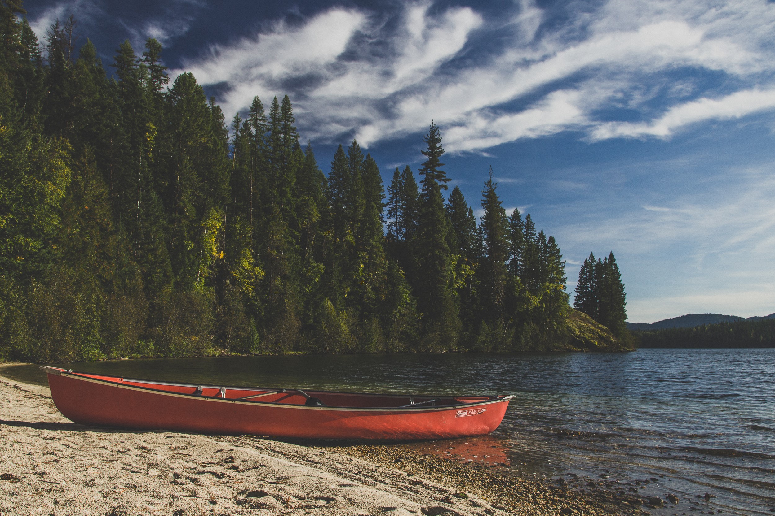 Red canoe on a sandy shore by a lake with trees HD Wallpaper