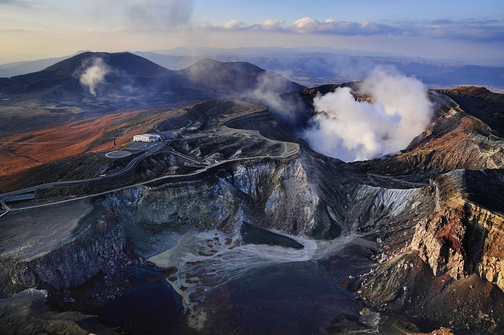 Volcanic crater with steam plumes and surrounding mountains HD Wallpaper