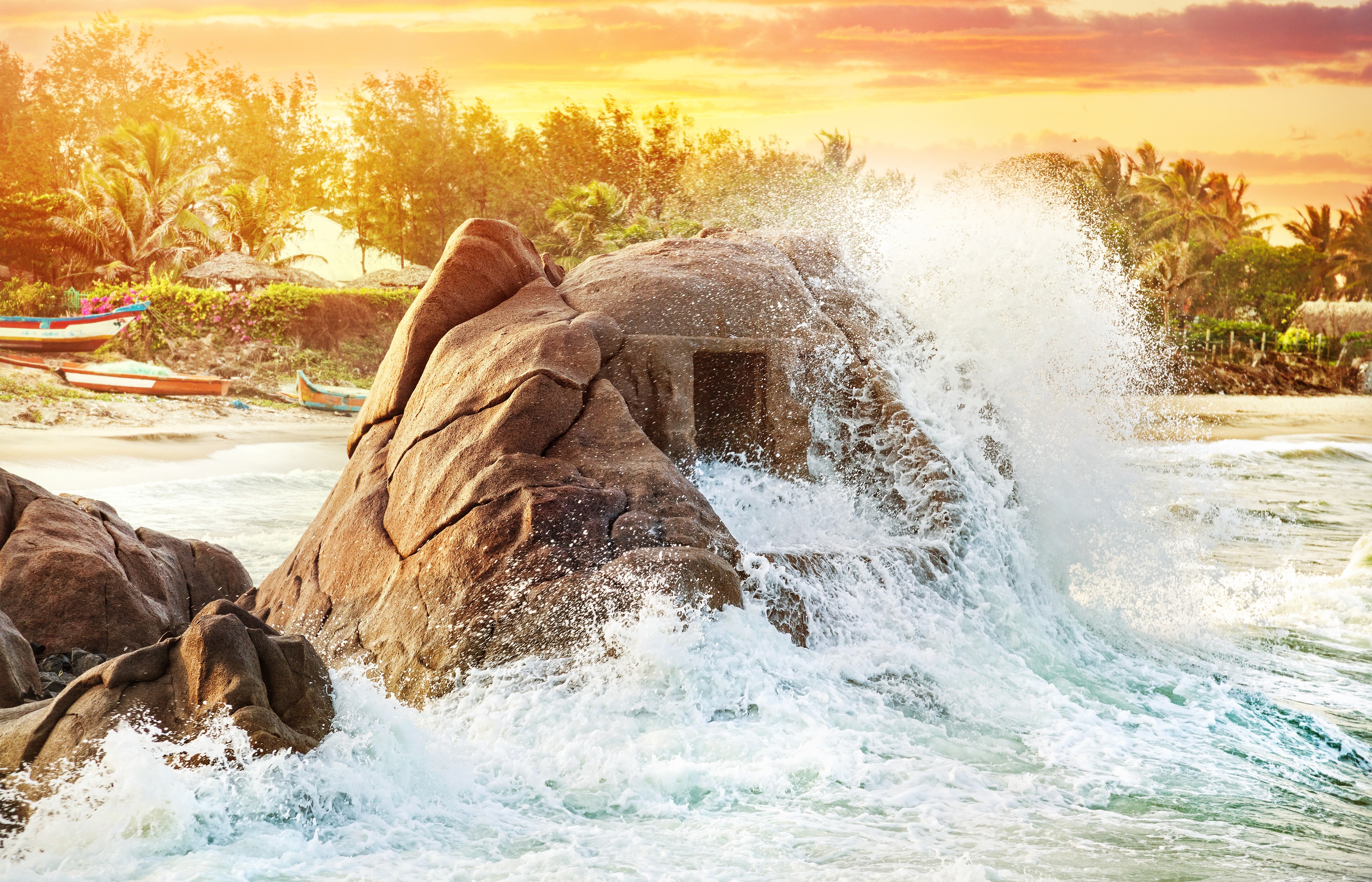 Wave crashing on rocks near a tropical beach at sunset HD Wallpaper