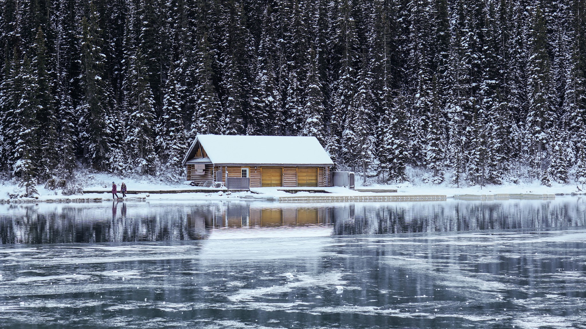 Wooden cabin by a frozen lake with pine forest in winter HD Wallpaper