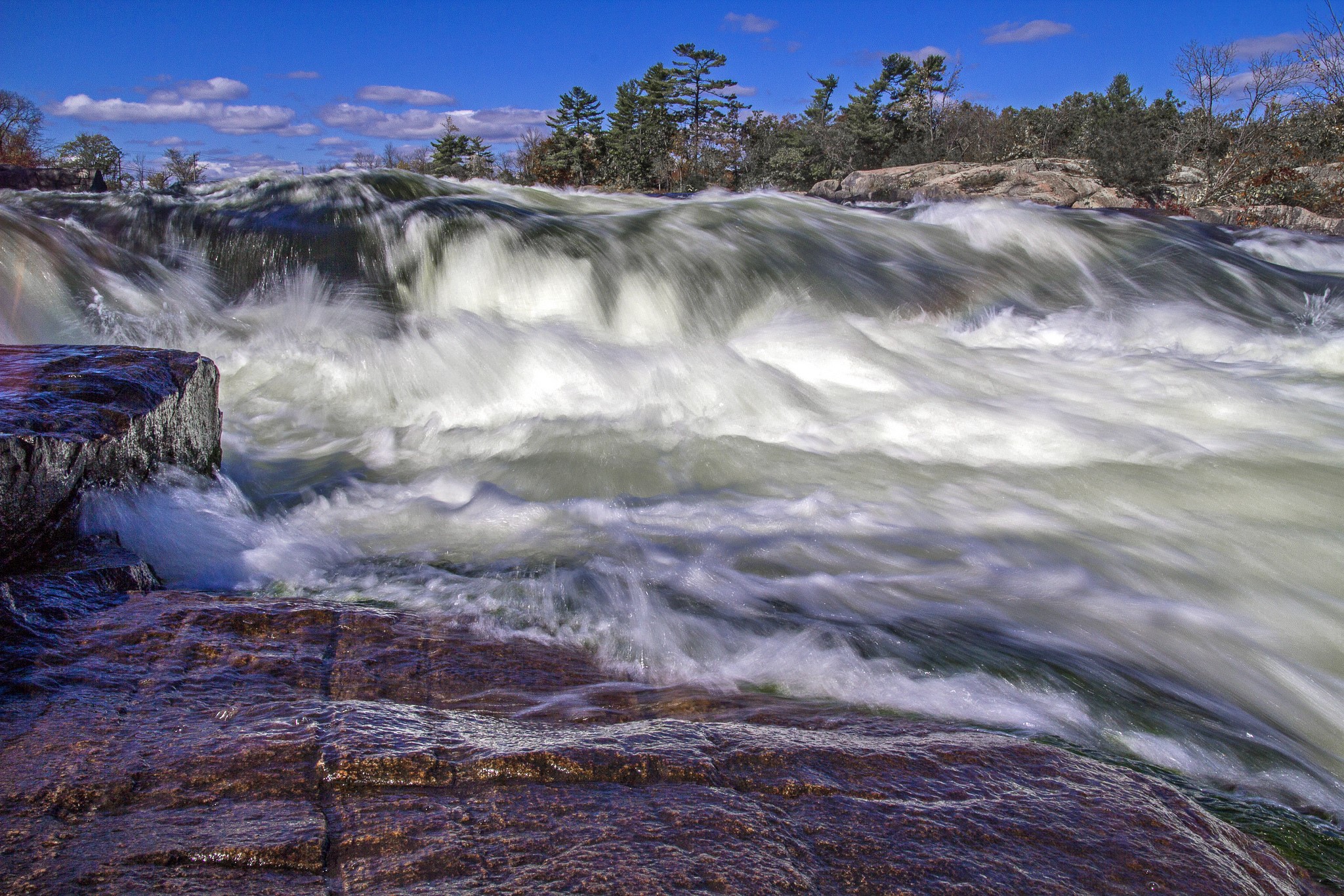 Fast-flowing river over rocks with trees in background HD Wallpaper