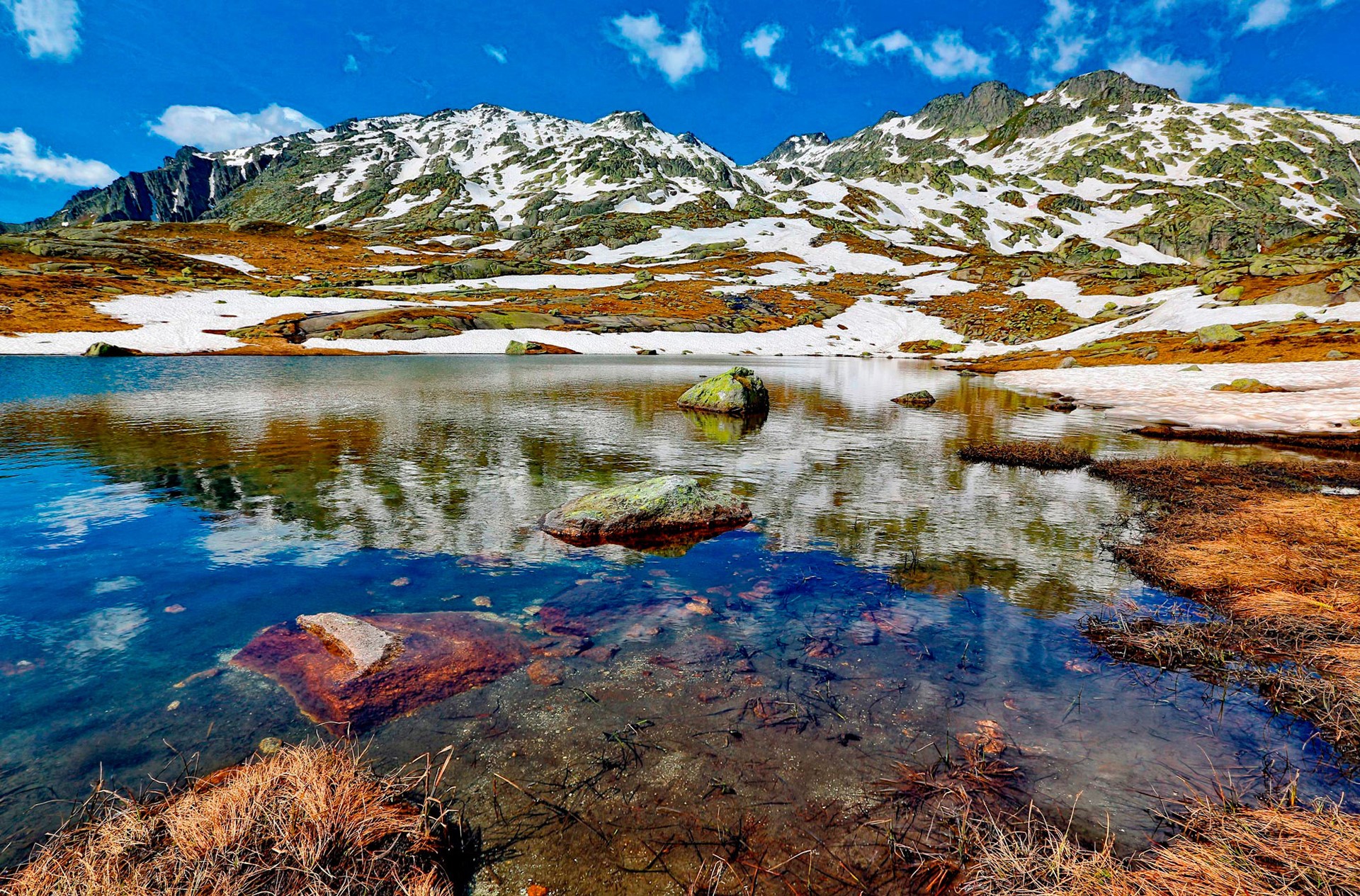 Snow-capped mountains reflected in a clear lake with rocks HD Wallpaper