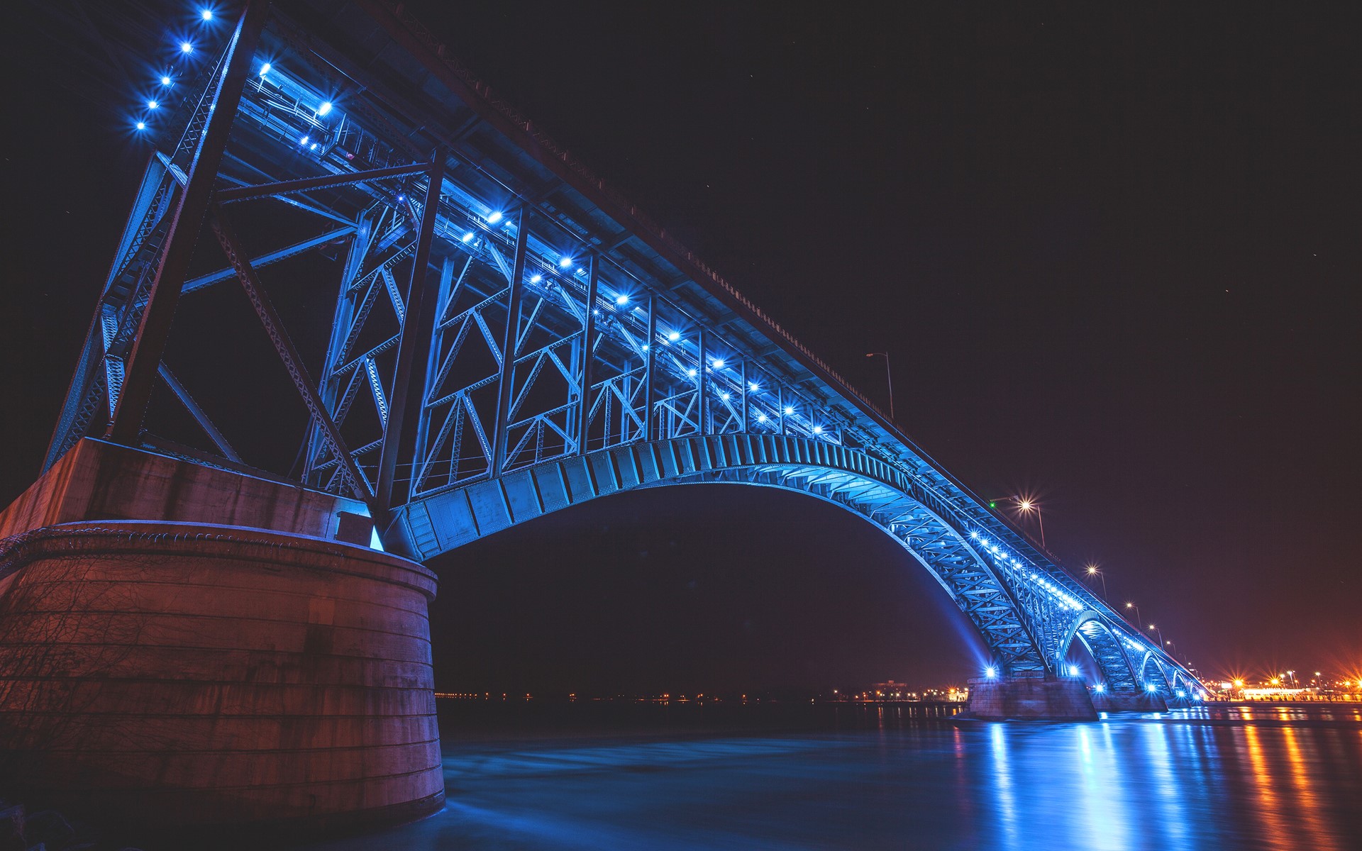 Bridge illuminated with blue lights at night over water HD Wallpaper