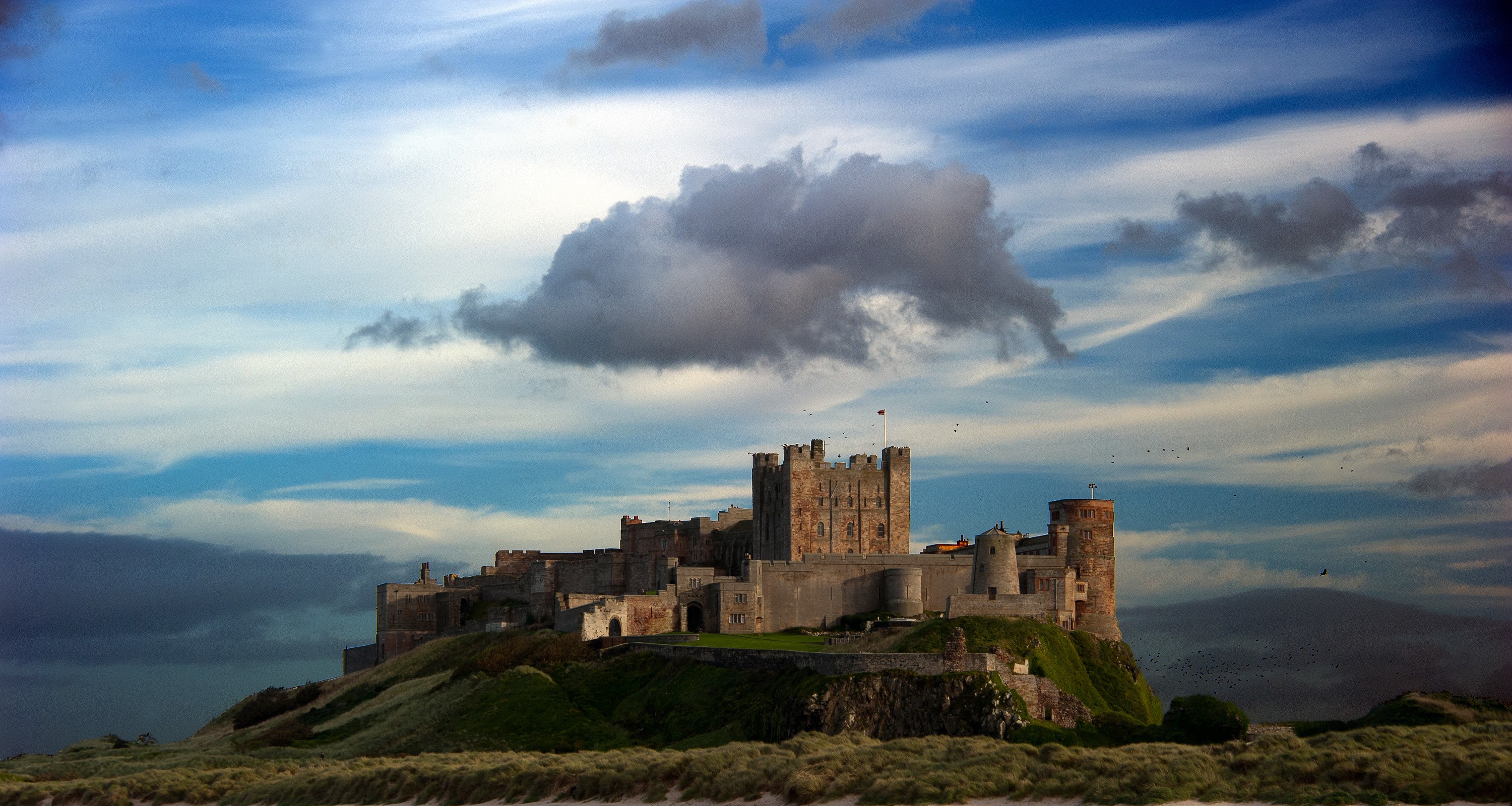 Bamburgh Castle on a grassy hill under a cloudy sky HD Wallpaper