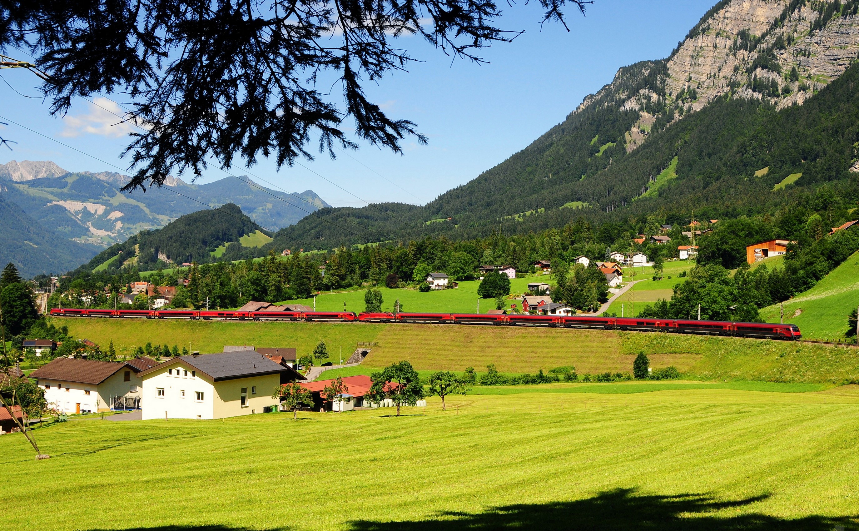 Red train passing through a village in the Austrian Alps HD Wallpaper