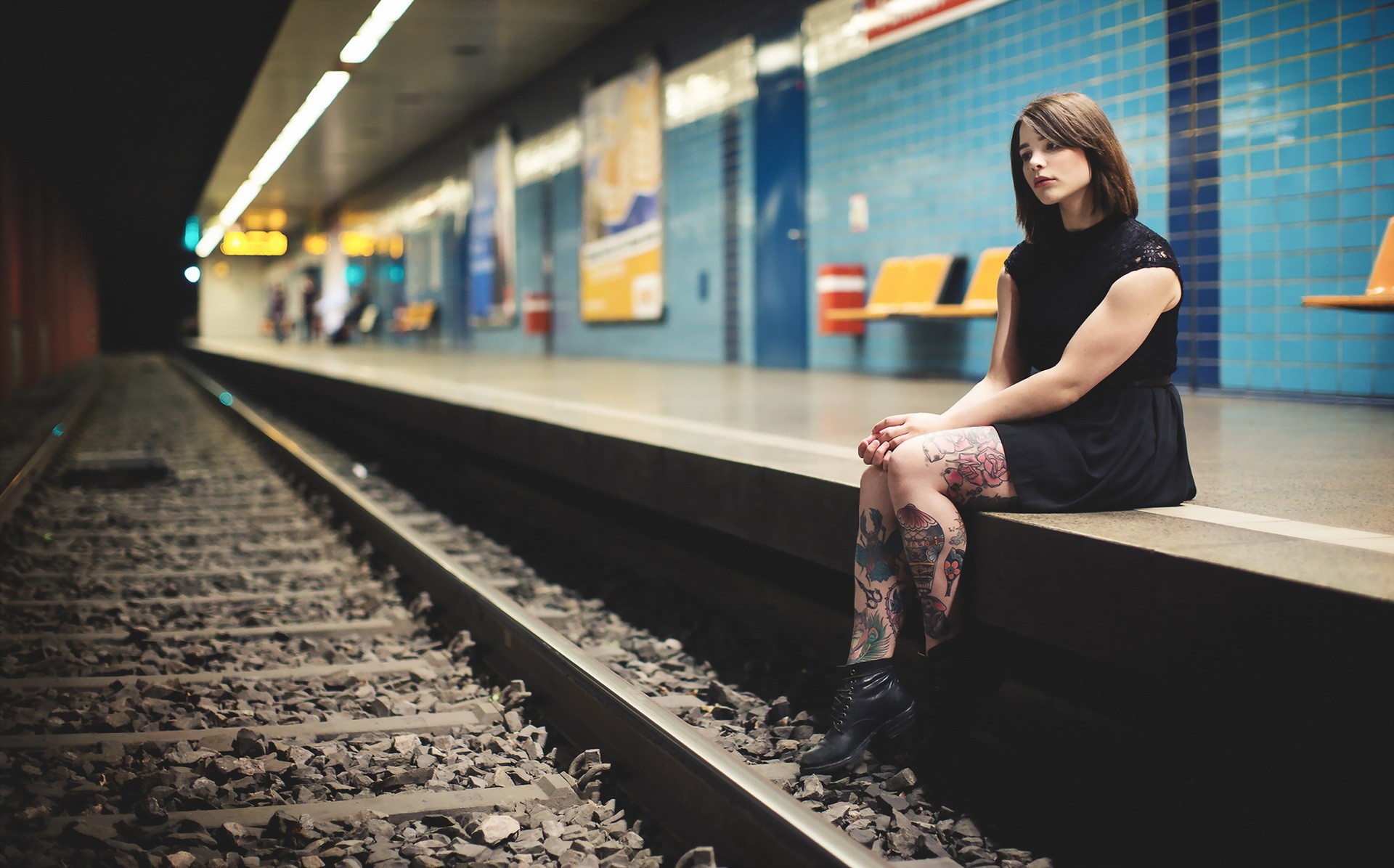 Woman with tattoos sitting on a subway platform HD Wallpaper