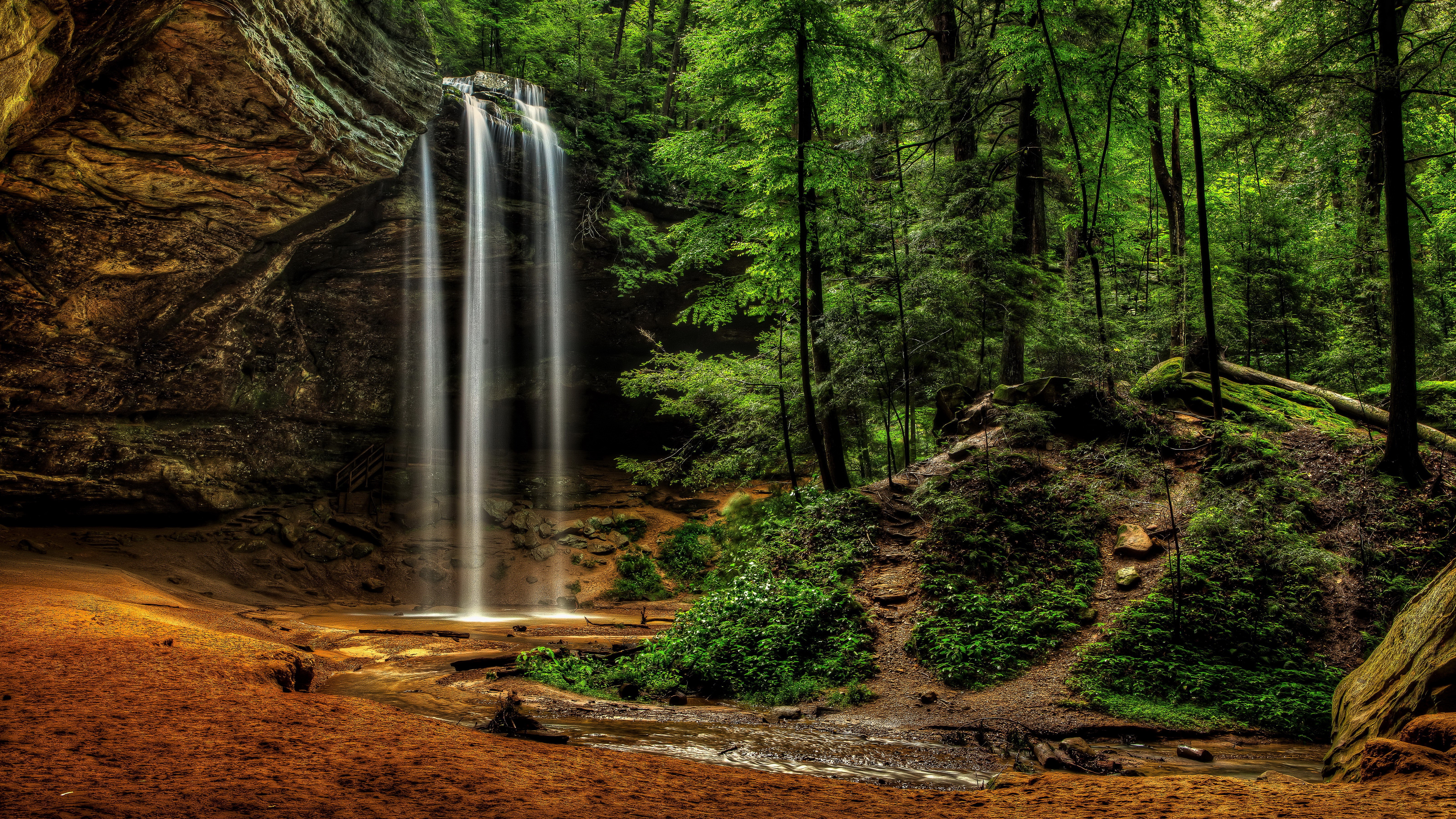 Waterfall in a lush green forest with rocky cliffs HD Wallpaper
