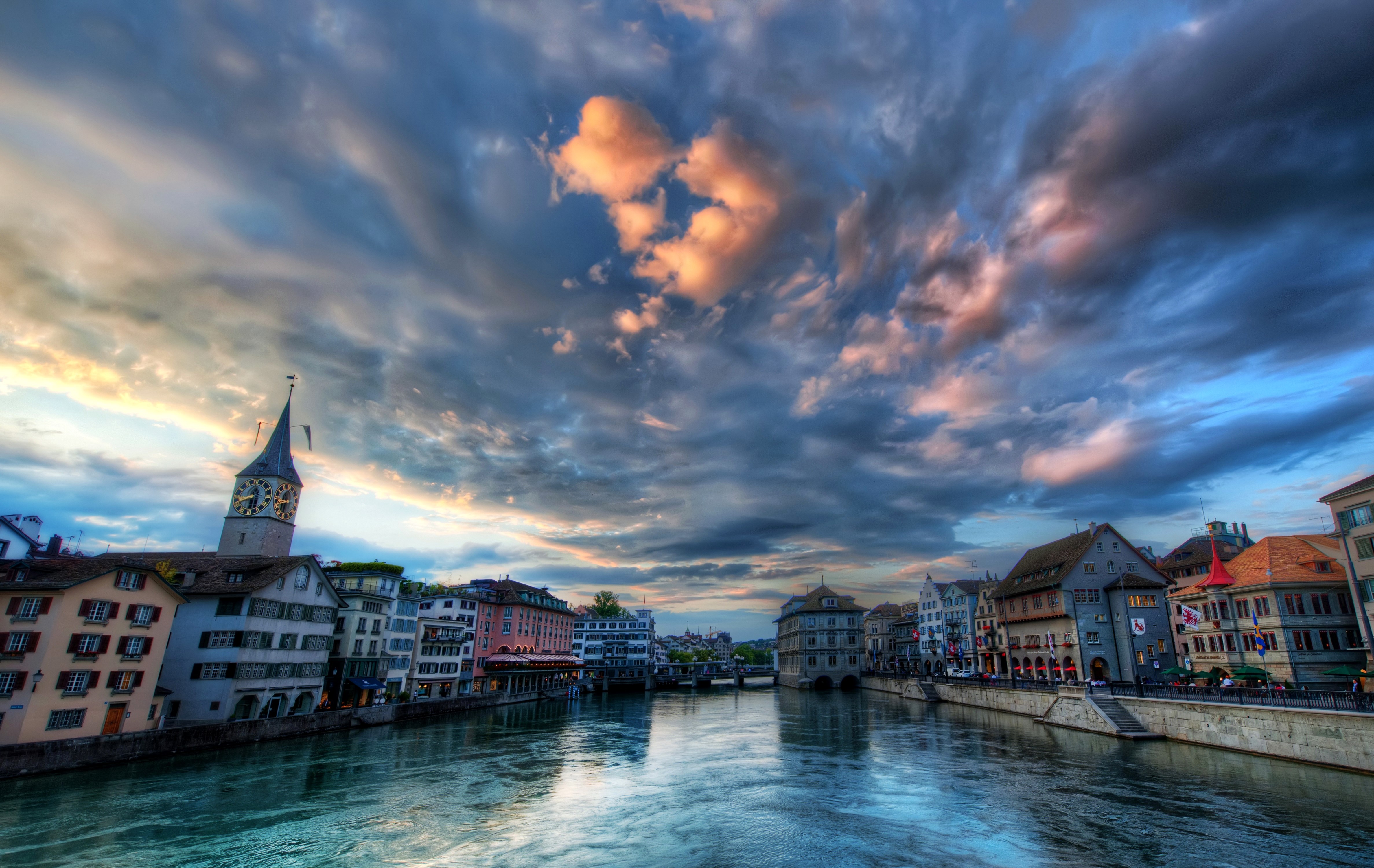 Zurich riverfront with clock tower and dramatic sky HD Wallpaper