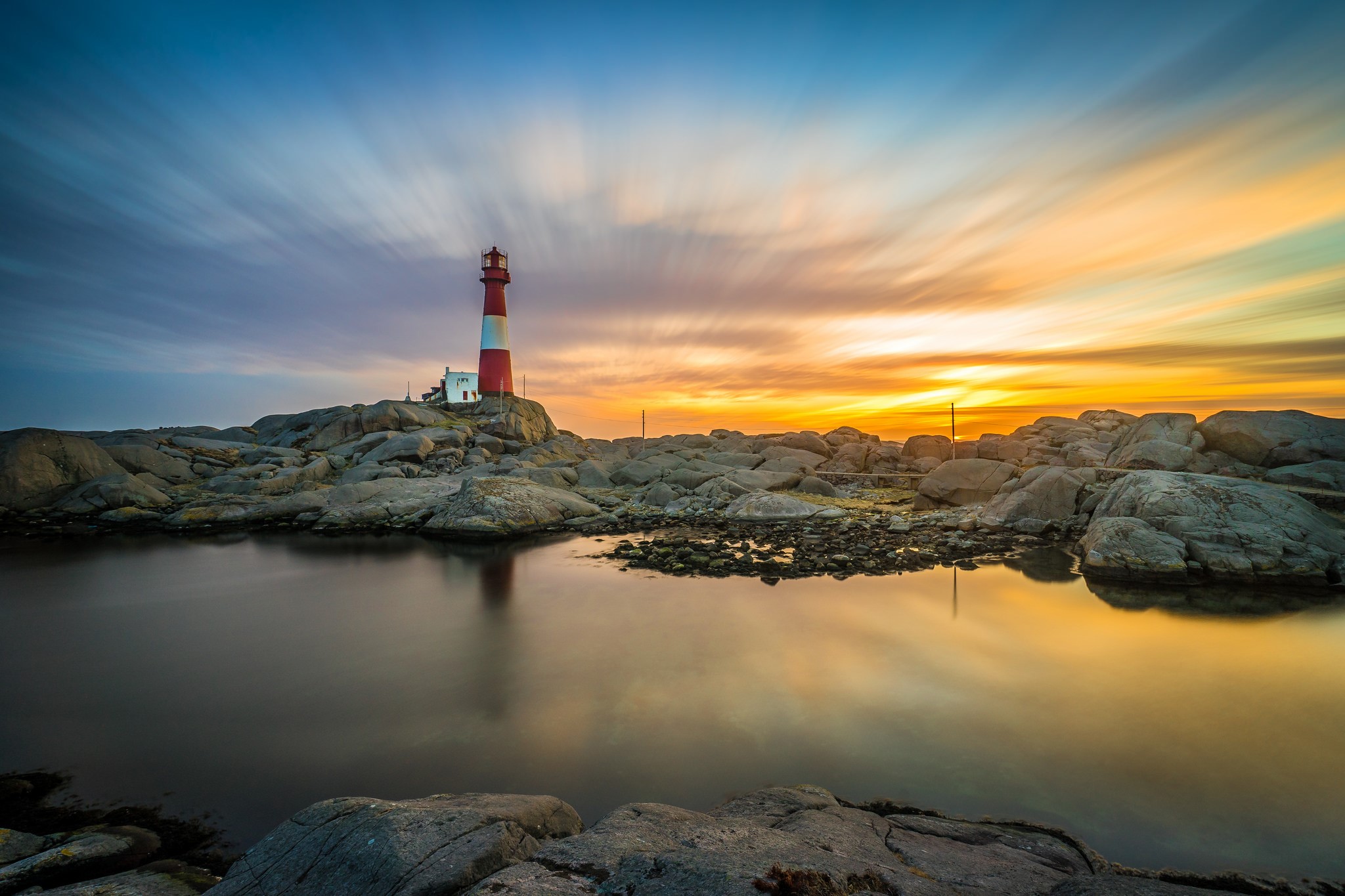 Red and white lighthouse on rocky shore at sunset HD Wallpaper