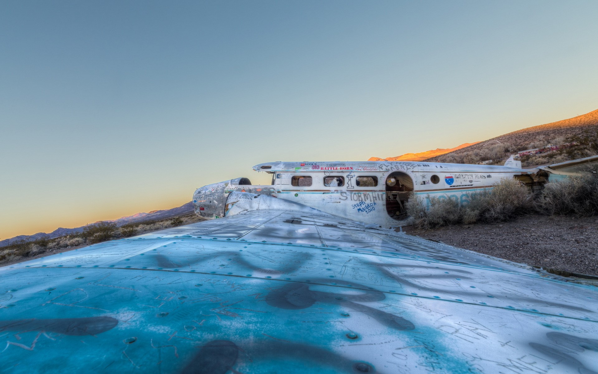 Graffiti-covered airplane wreck in desert landscape HD Wallpaper