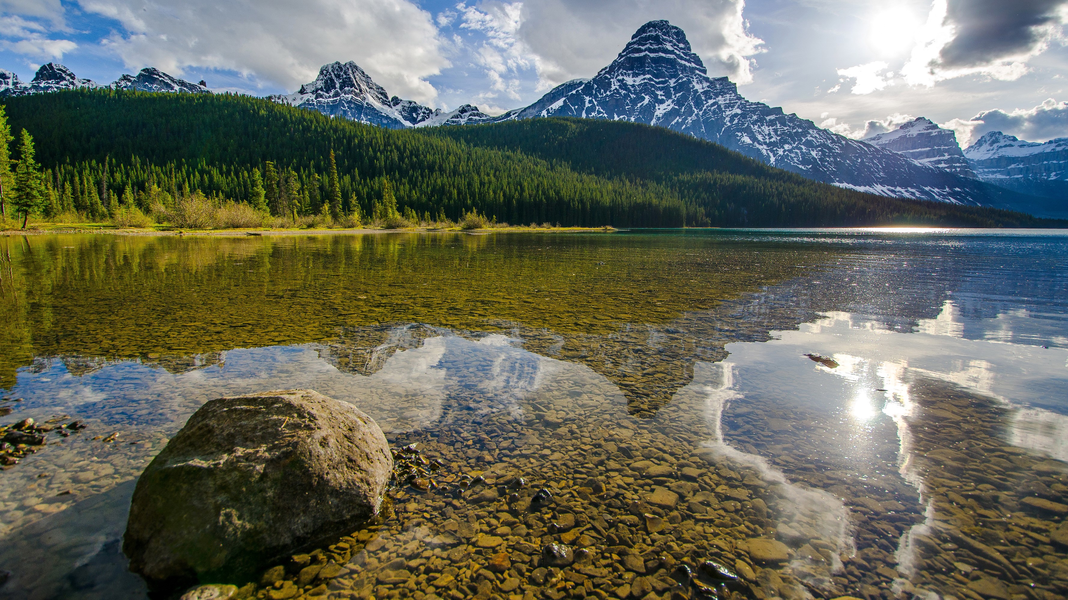 Mountains reflected in a clear lake with stones in the foreground HD Wallpaper