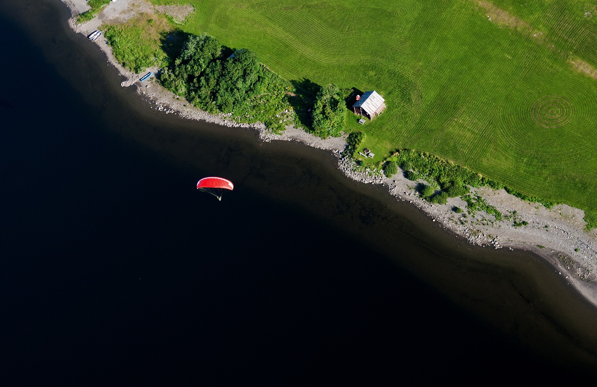 Paraglider flying over a dark lake near a grassy shore HD Wallpaper