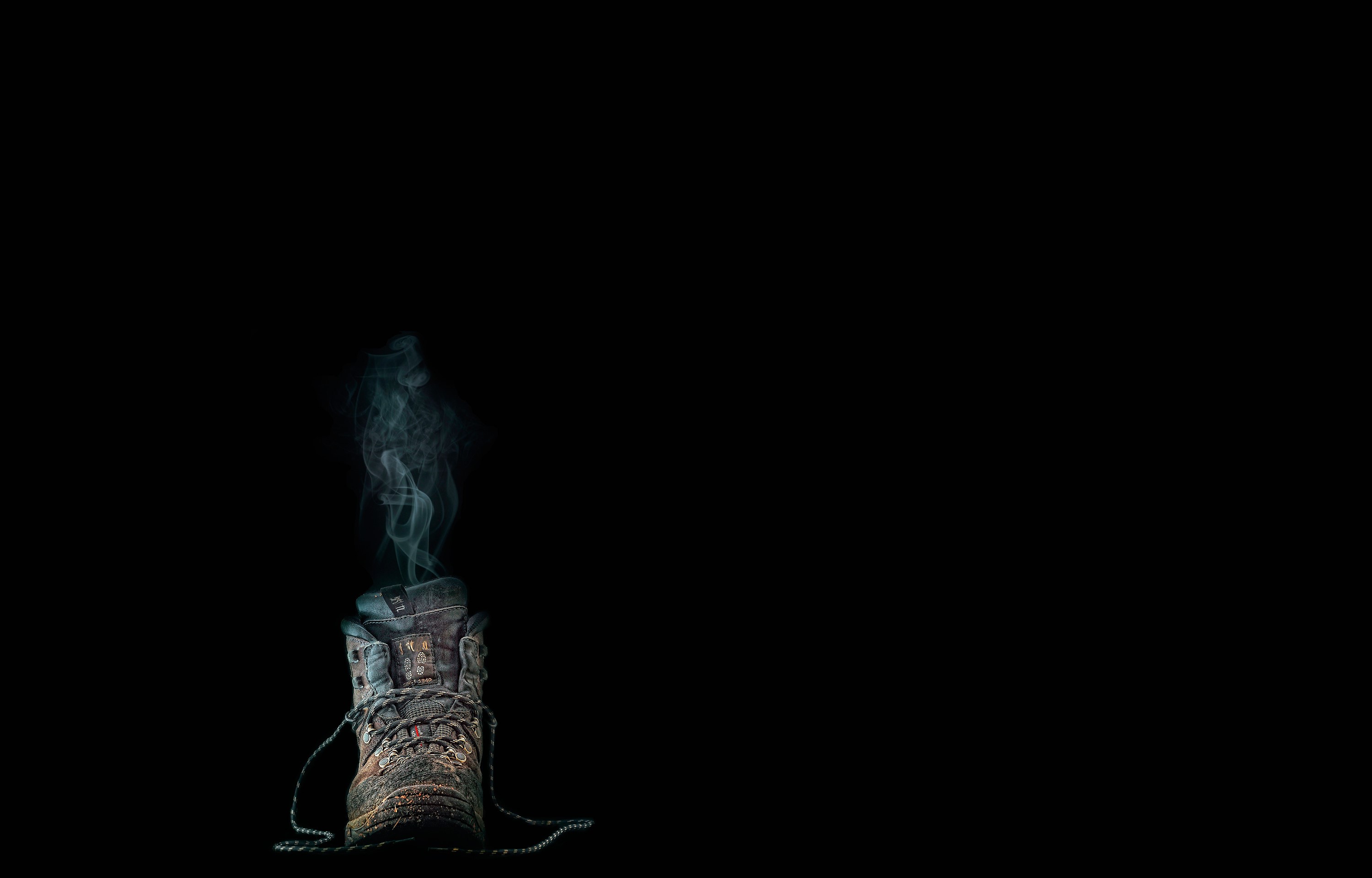 A worn hiking boot emitting smoke against a black background HD Wallpaper