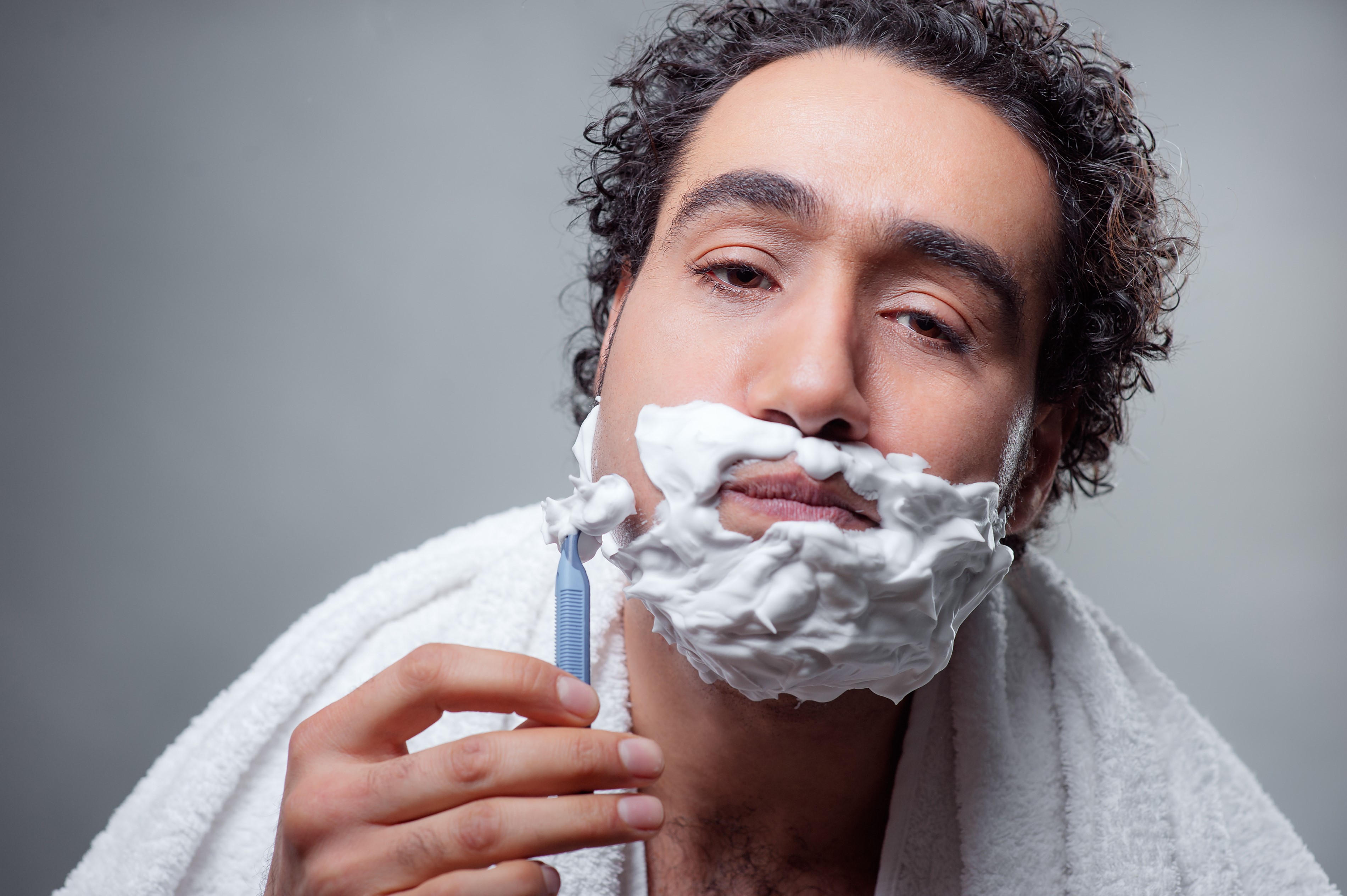 Man with curly hair shaving his face with a razor HD Wallpaper