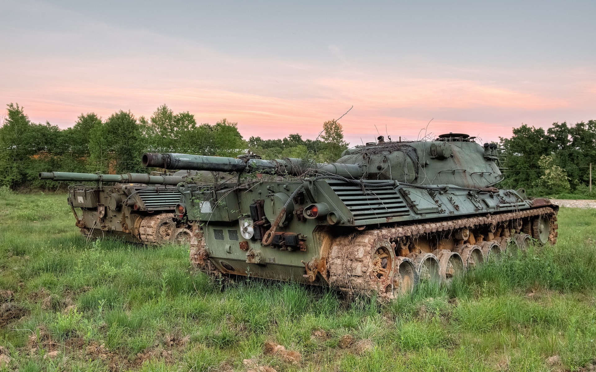 Two abandoned tanks in a grassy field at sunset HD Wallpaper