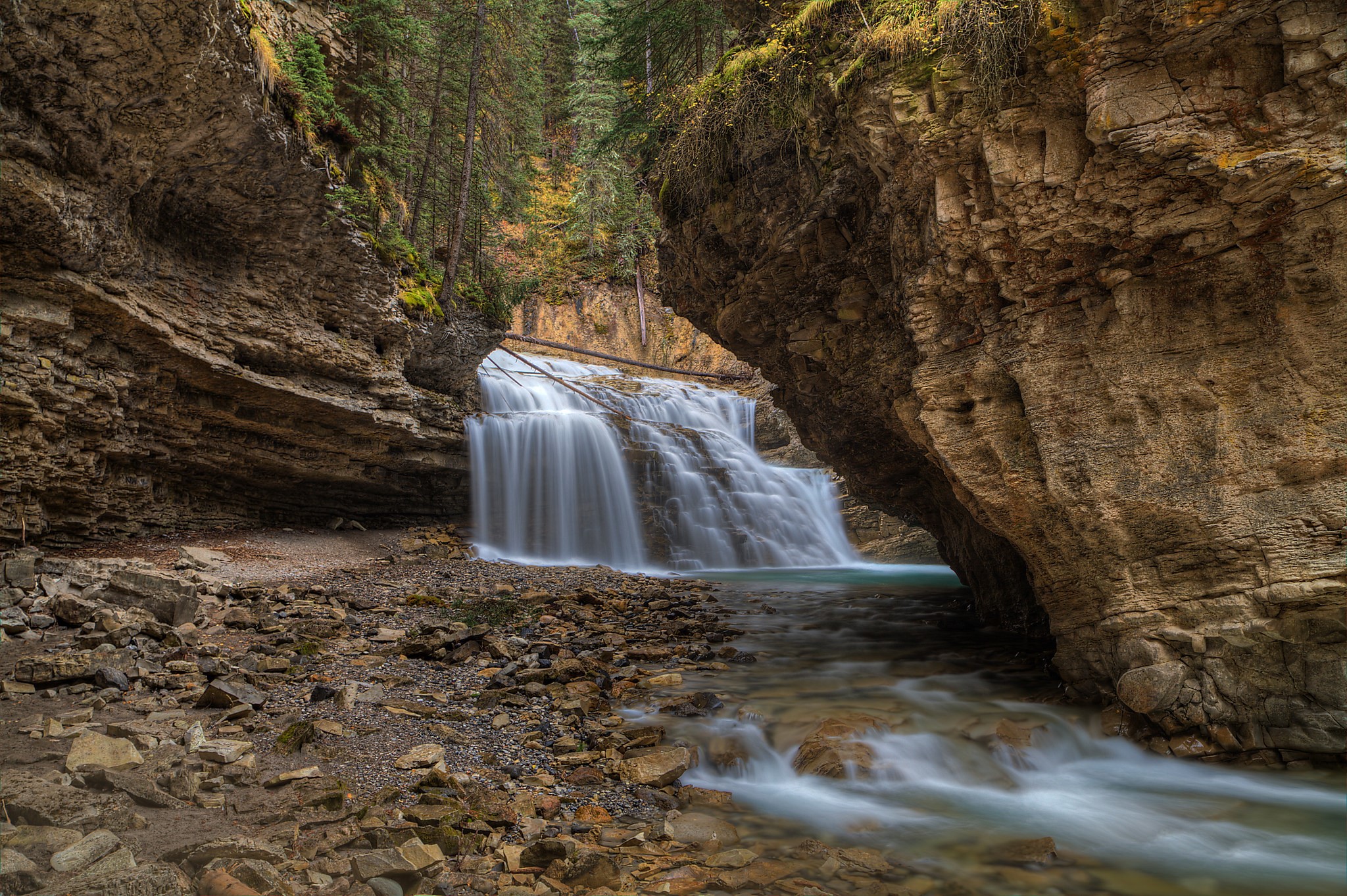 Waterfall cascading through a rocky canyon with trees HD Wallpaper