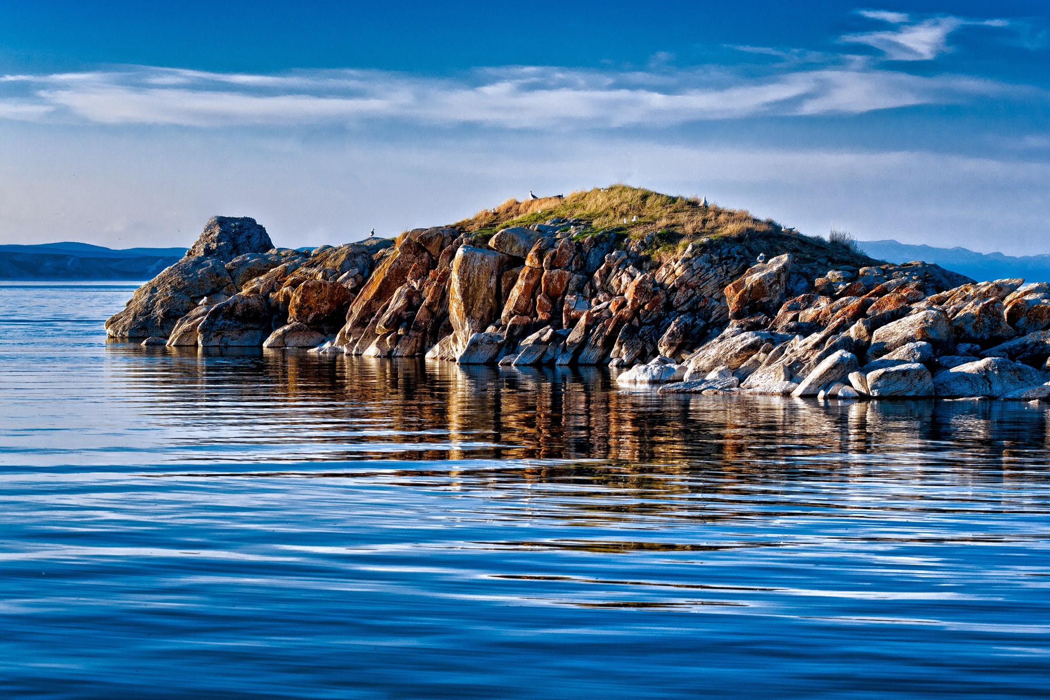 Rocky island in a blue lake under a cloudy sky HD Wallpaper