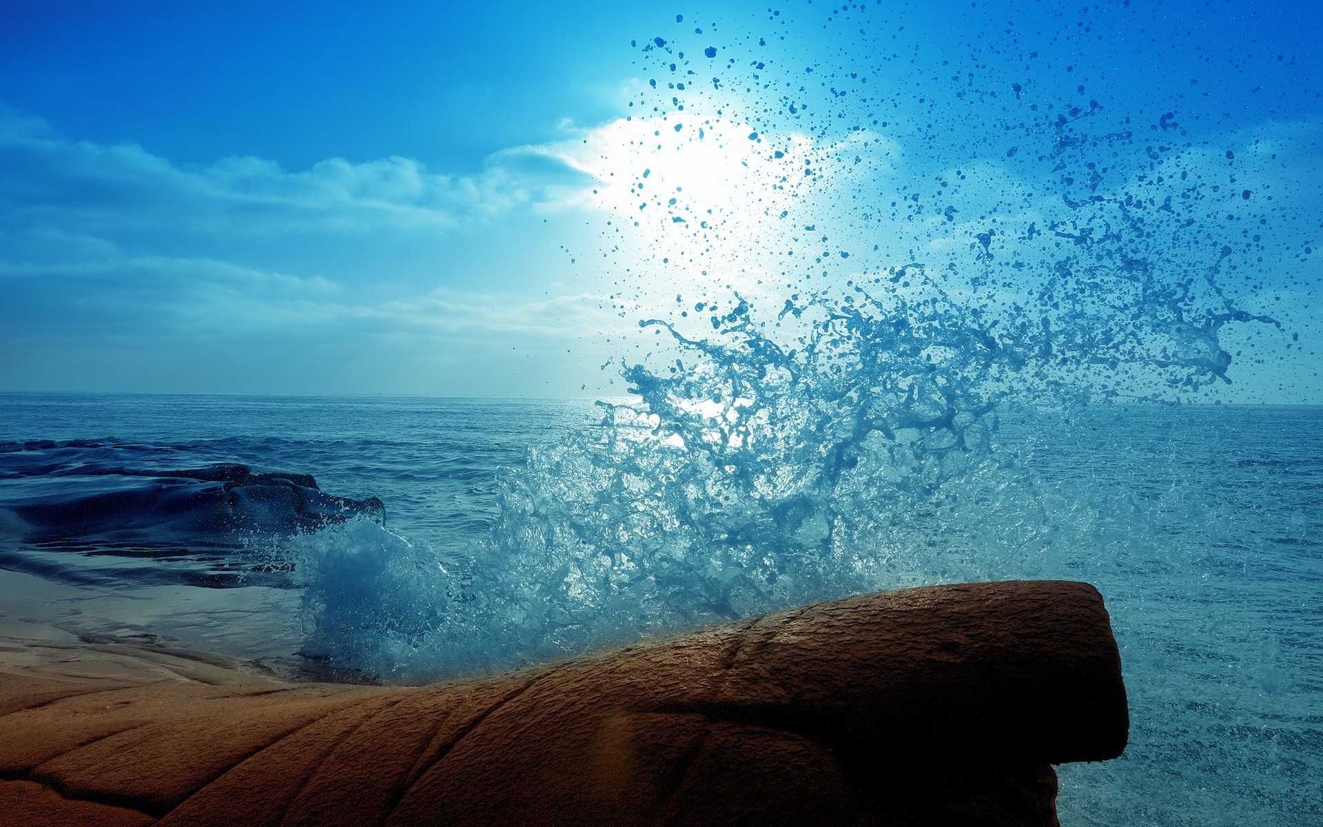 Ocean wave crashing on rocks under a bright sun HD Wallpaper