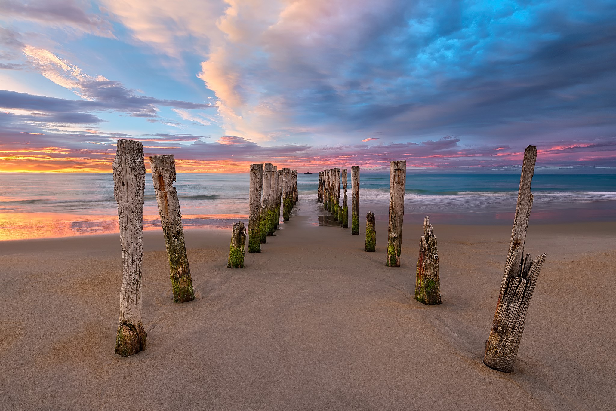 Old wooden posts on a beach at sunset HD Wallpaper