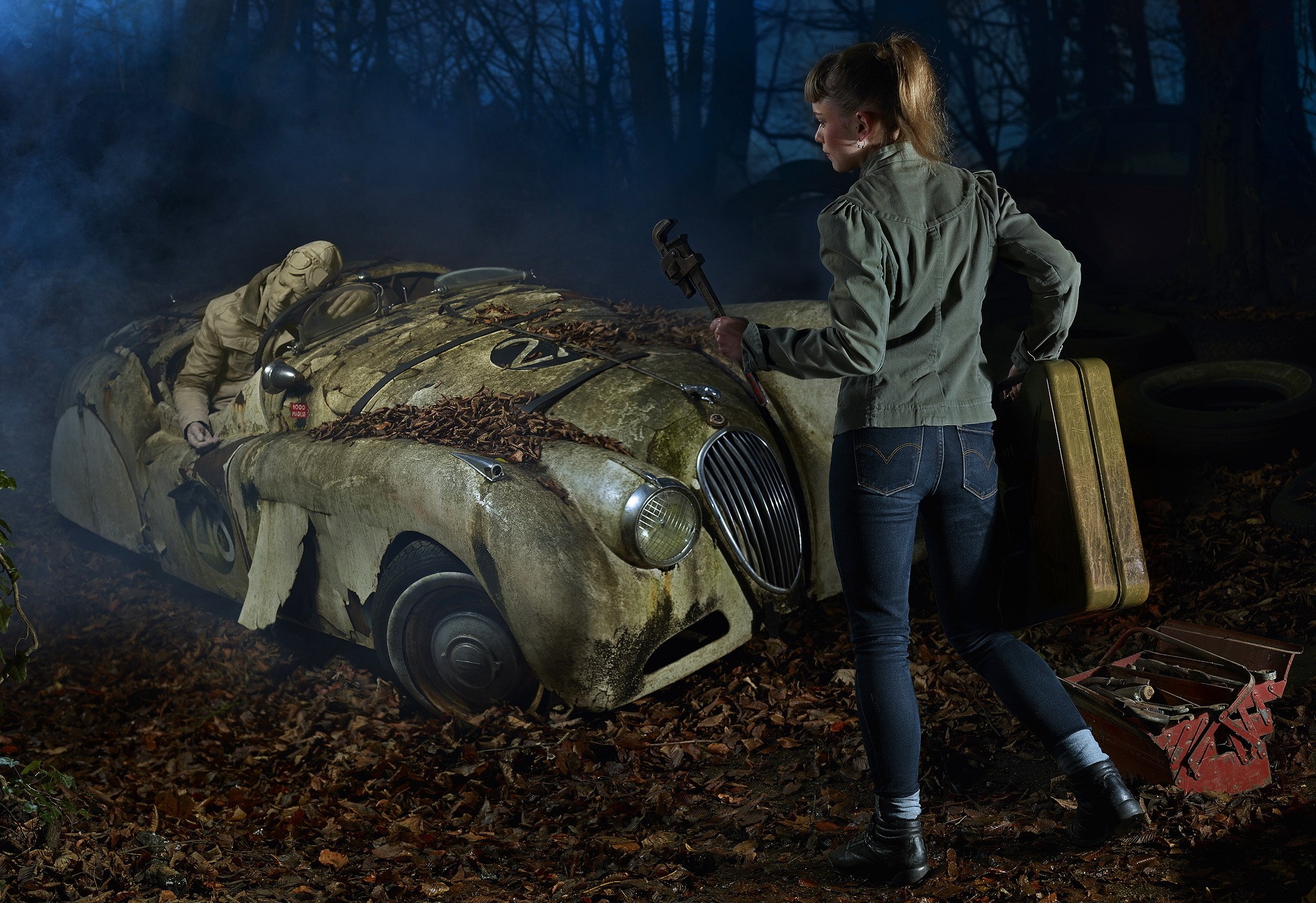 Woman with suitcase and wrench near abandoned car in forest HD Wallpaper