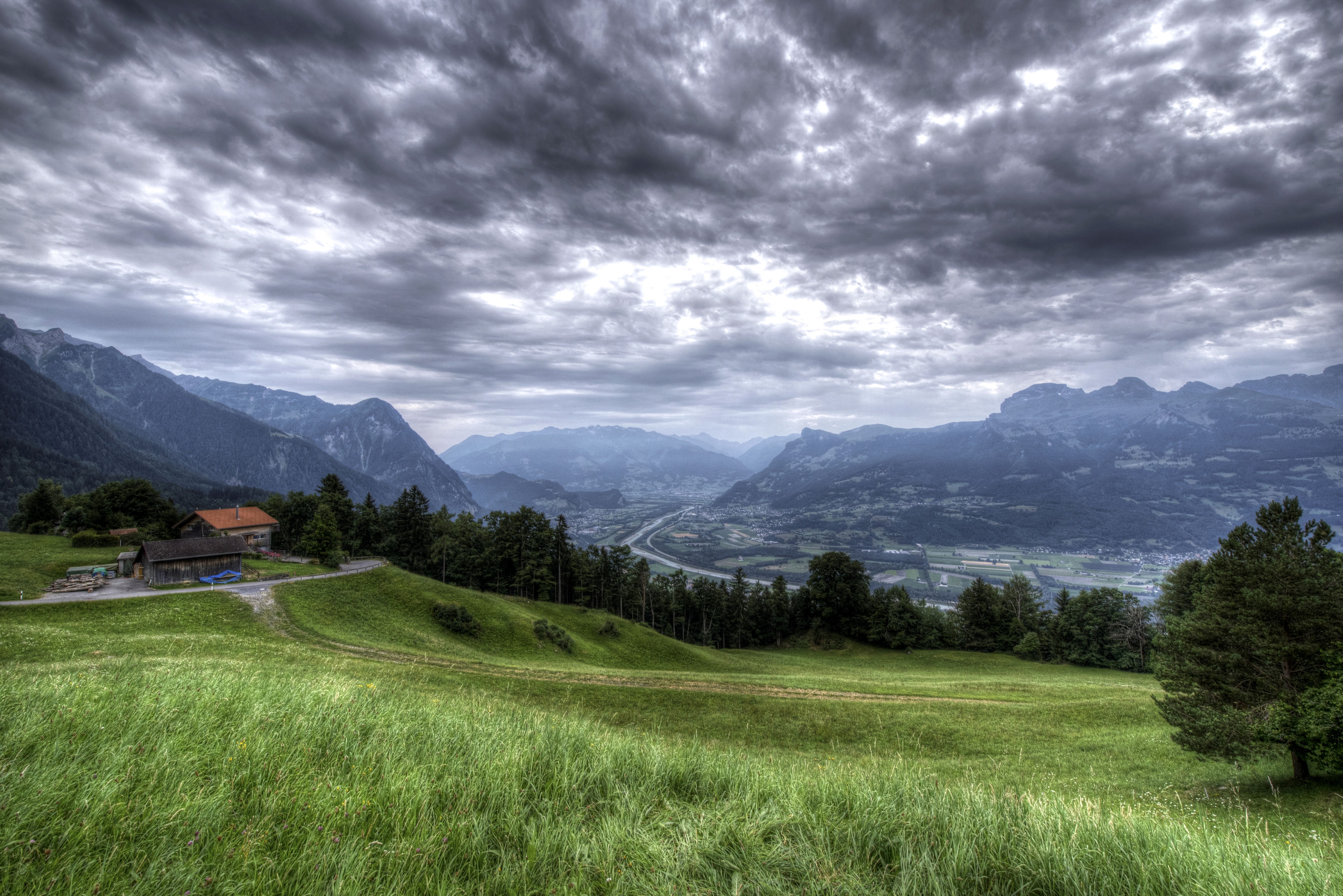 Mountains and valley with houses and cloudy sky HD Wallpaper