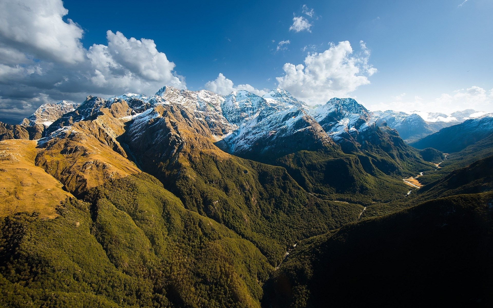 Snow-capped mountains and forested valley under a blue sky HD Wallpaper