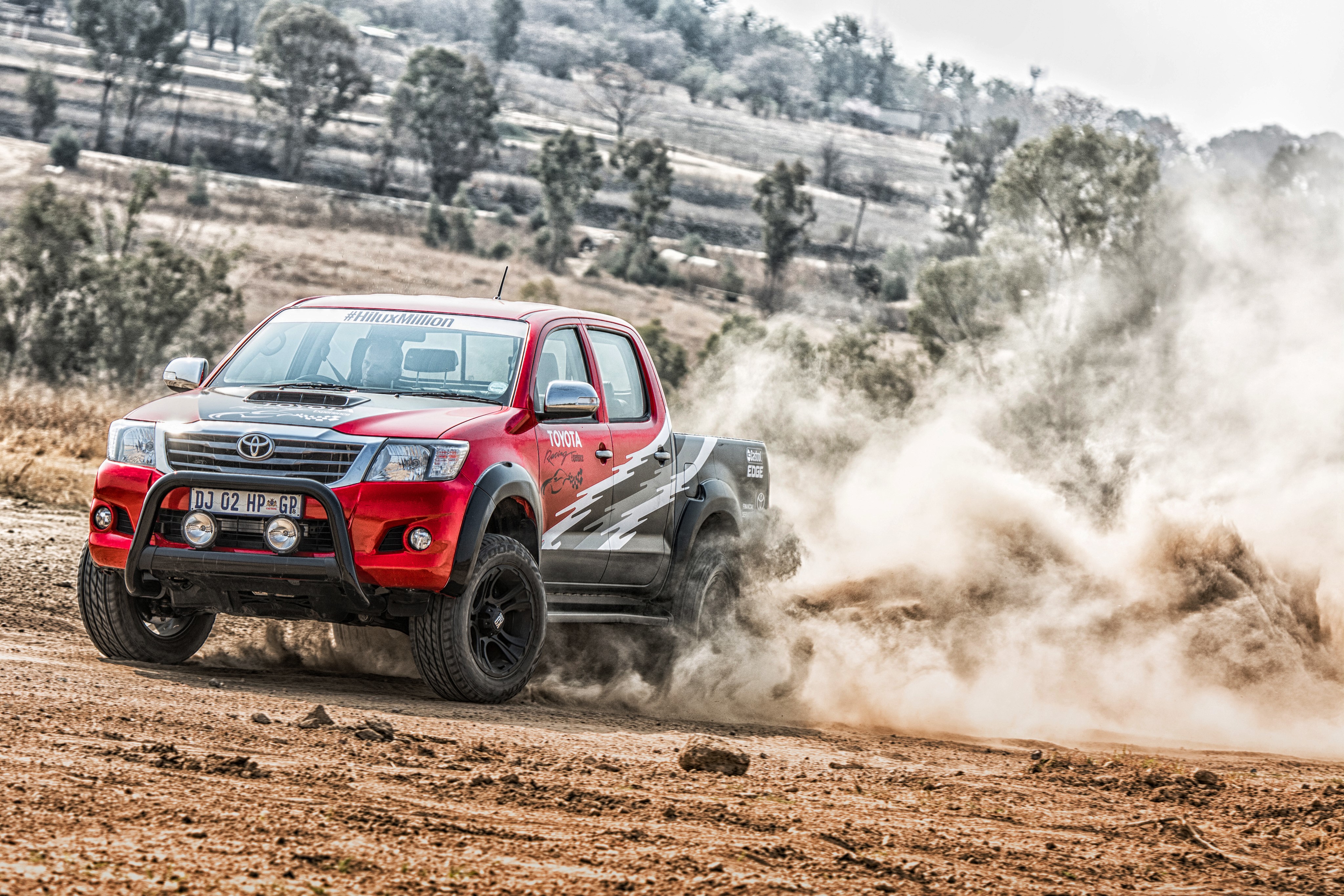 Red Toyota Hilux driving through dust HD Wallpaper