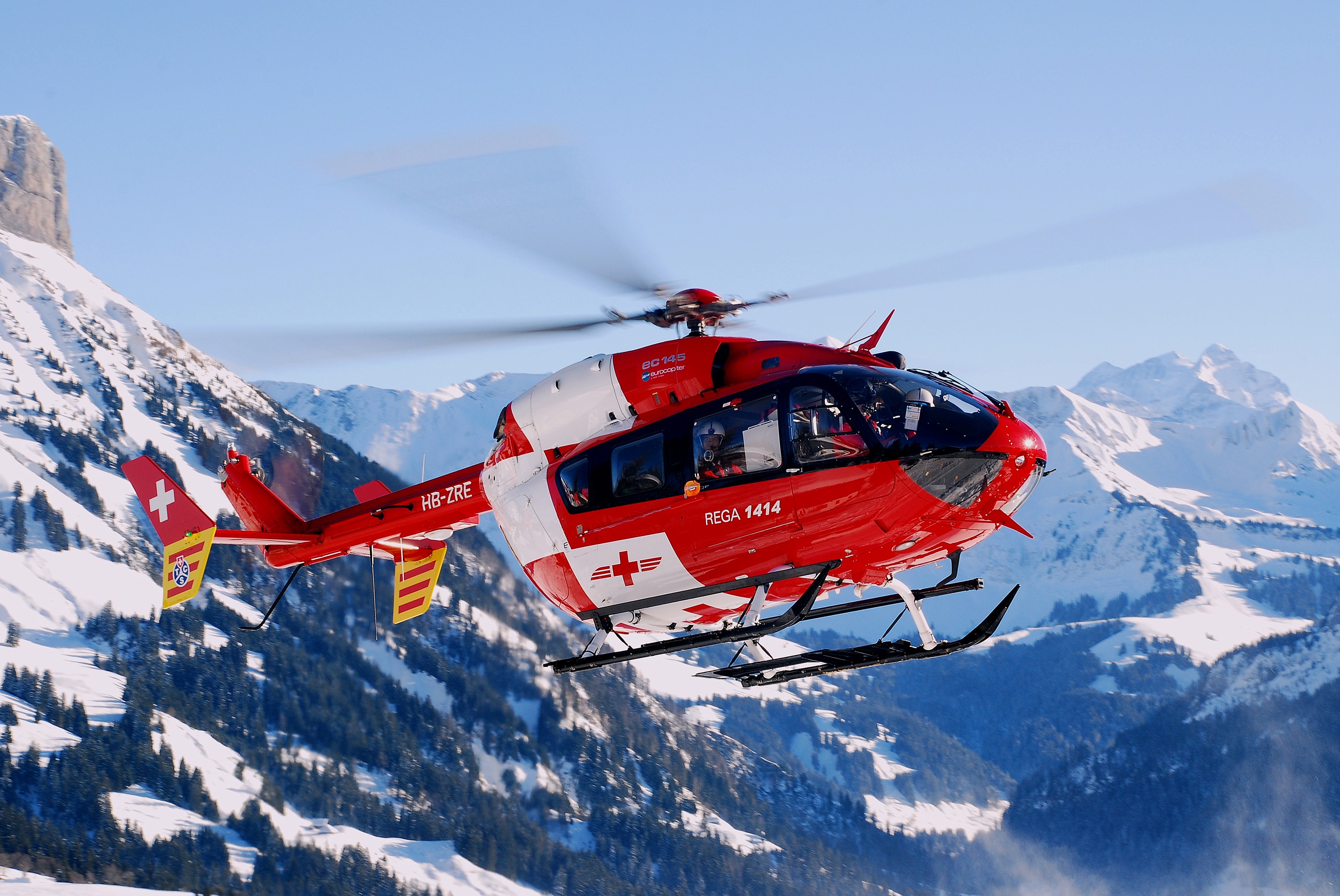 Red REGA helicopter flying over snowy mountains HD Wallpaper