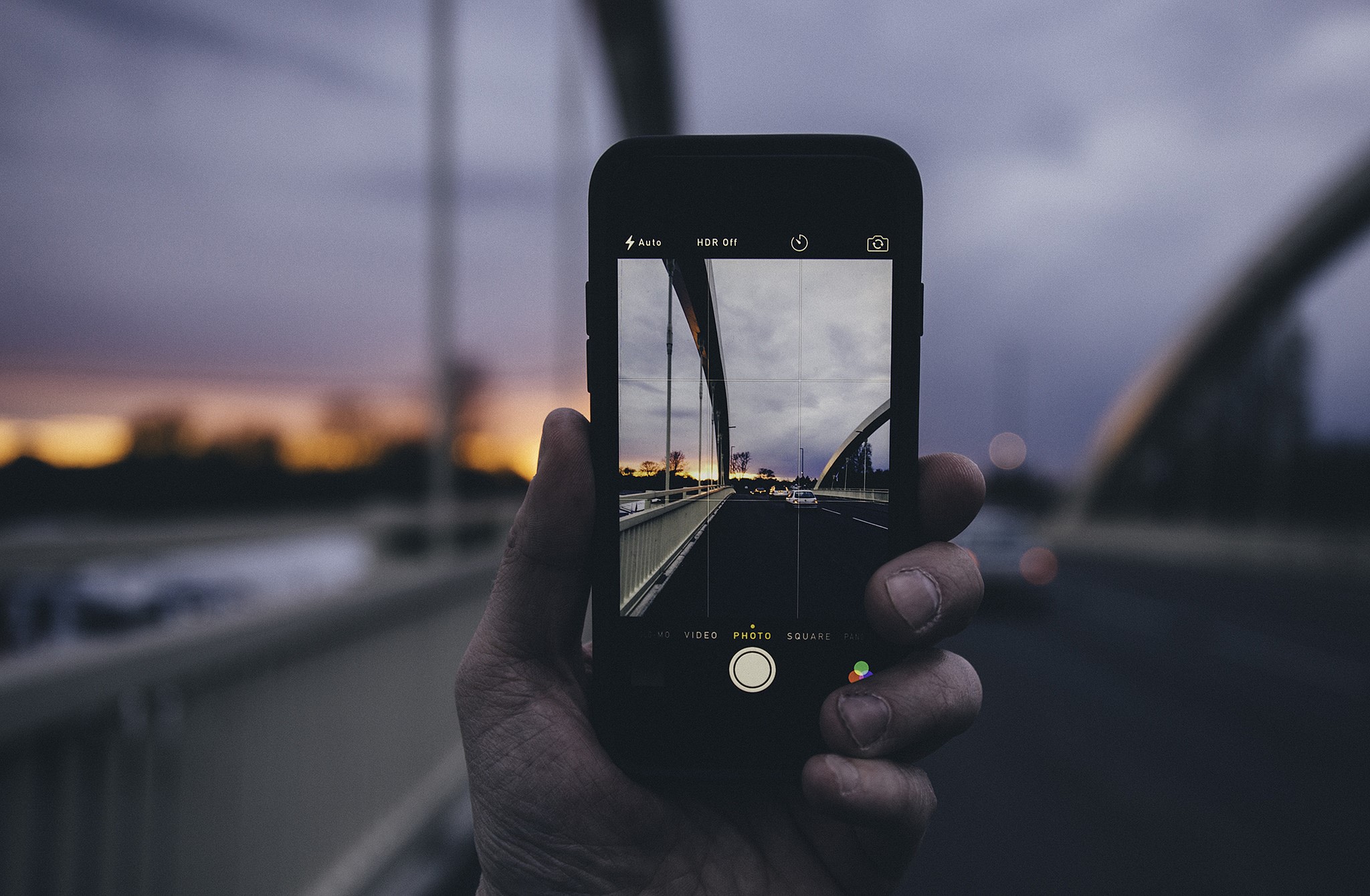 Hand holding iPhone taking picture of bridge at sunset HD Wallpaper