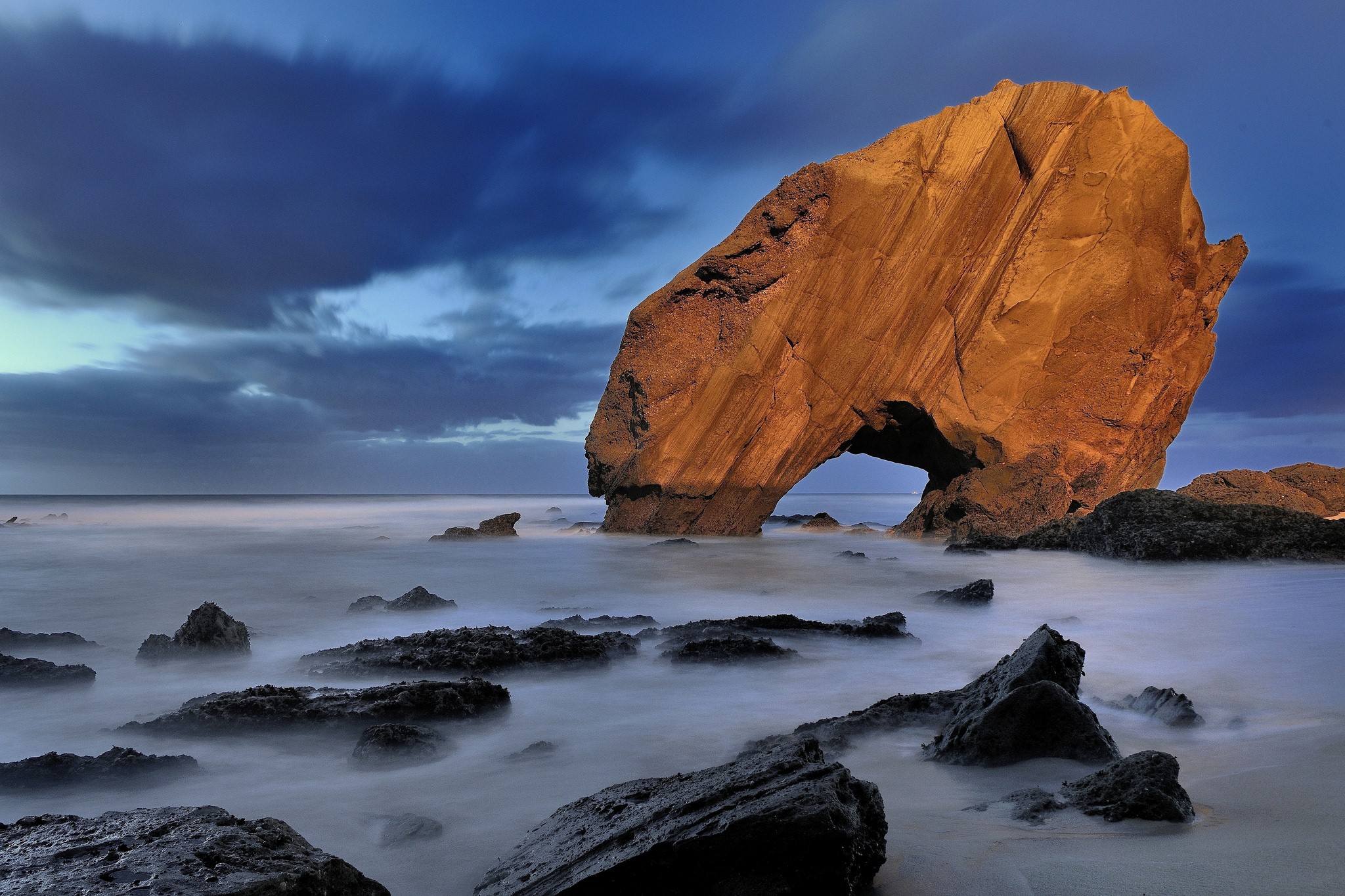 Arch rock formation on a rocky beach at dusk HD Wallpaper