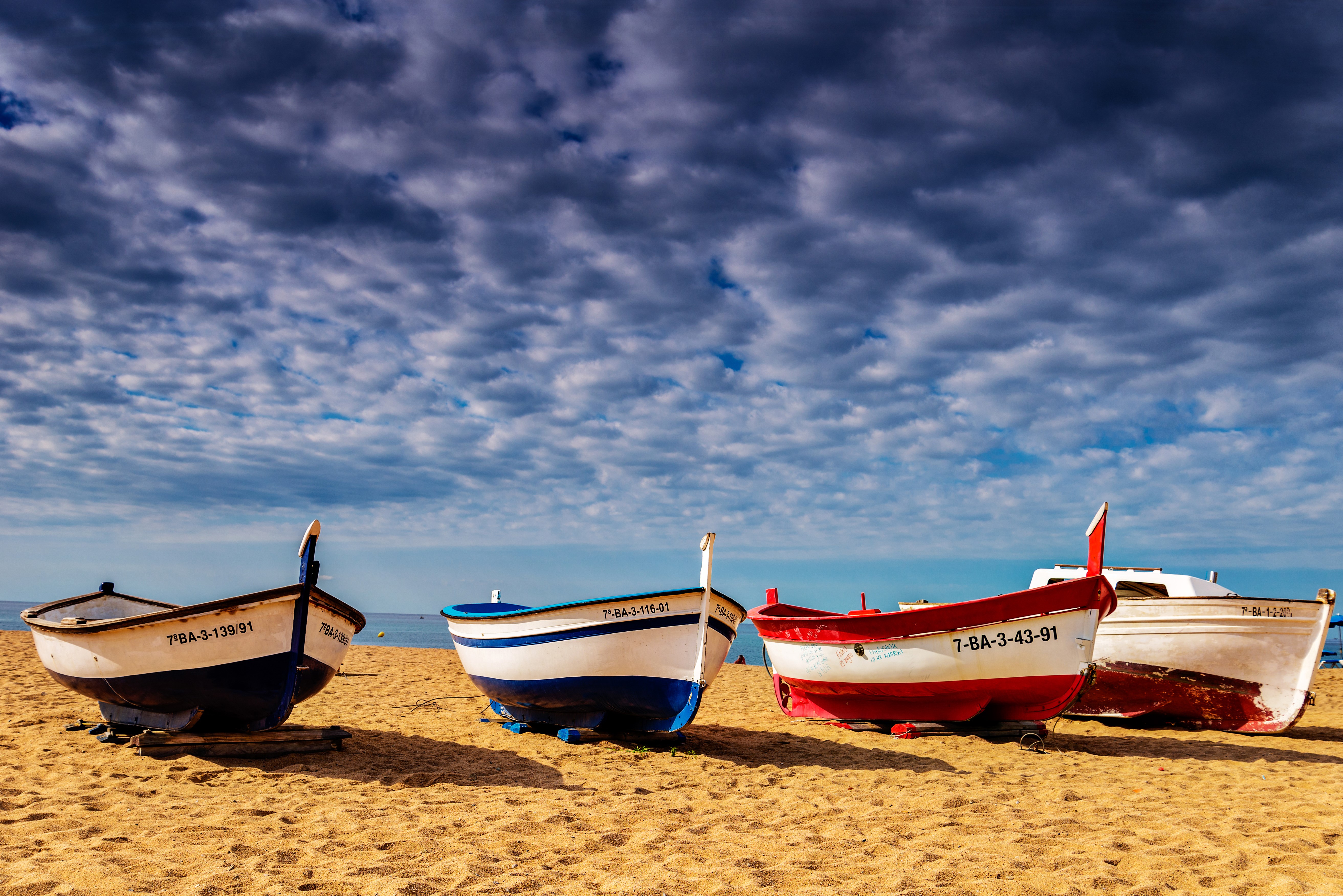 Four fishing boats on a sandy beach under a cloudy sky HD Wallpaper
