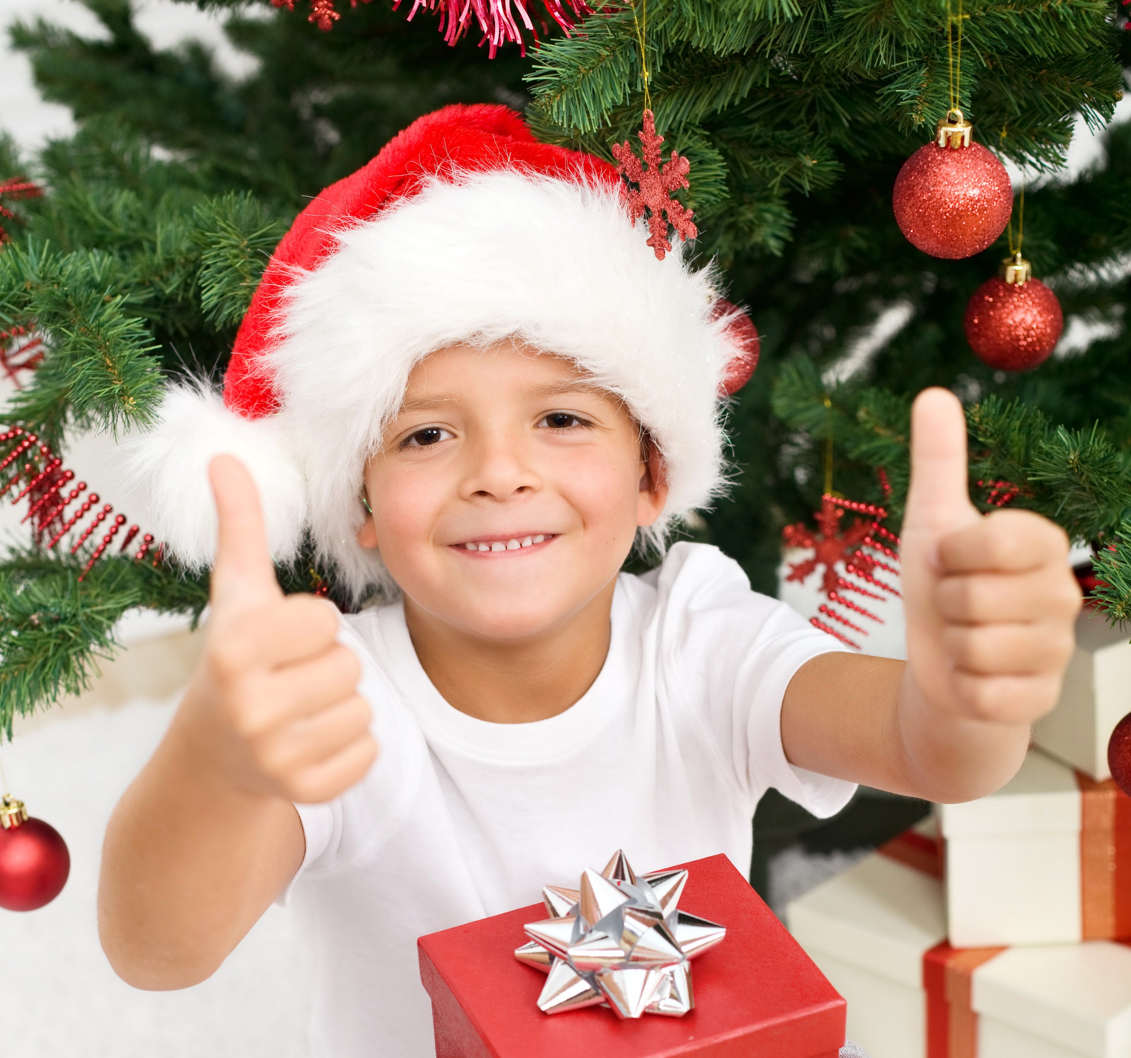Boy in Santa hat giving thumbs up by Christmas tree HD Wallpaper